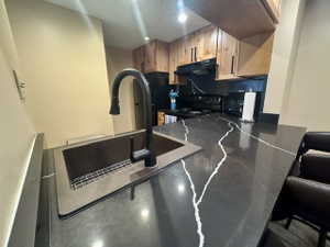 Kitchen featuring dark countertops with white veining, a matte black gooseneck faucet, an undermount sink, recessed lighting, and wood-finish cabinetry with black hardware