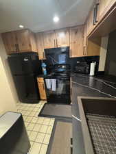 Kitchen featuring black appliances, wood cabinetry, black countertops with white veining, and a large single-basin sink