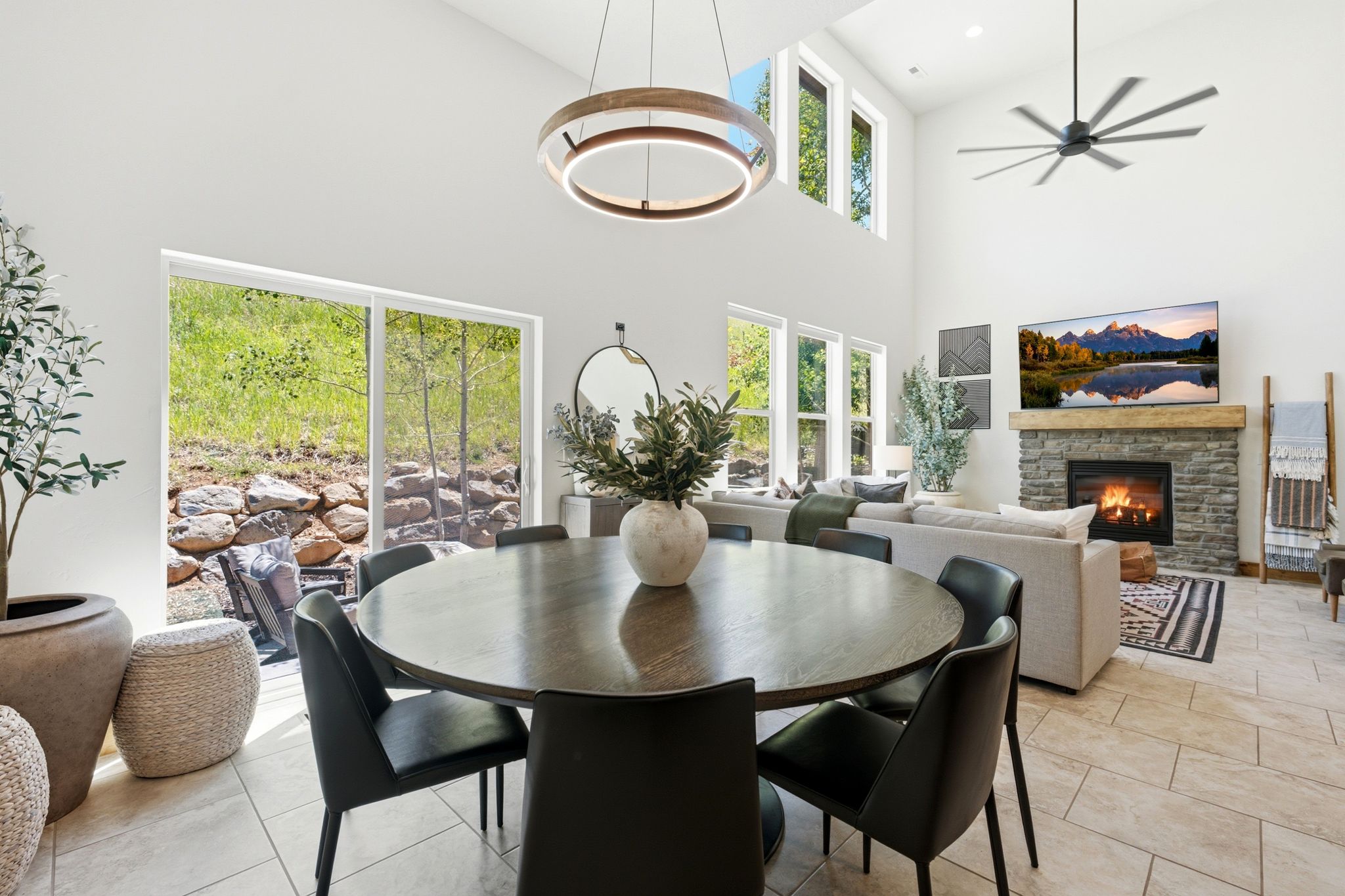 Open-concept living space featuring a stone-clad fireplace with a wood mantel, high vaulted ceilings, and large format tile flooring