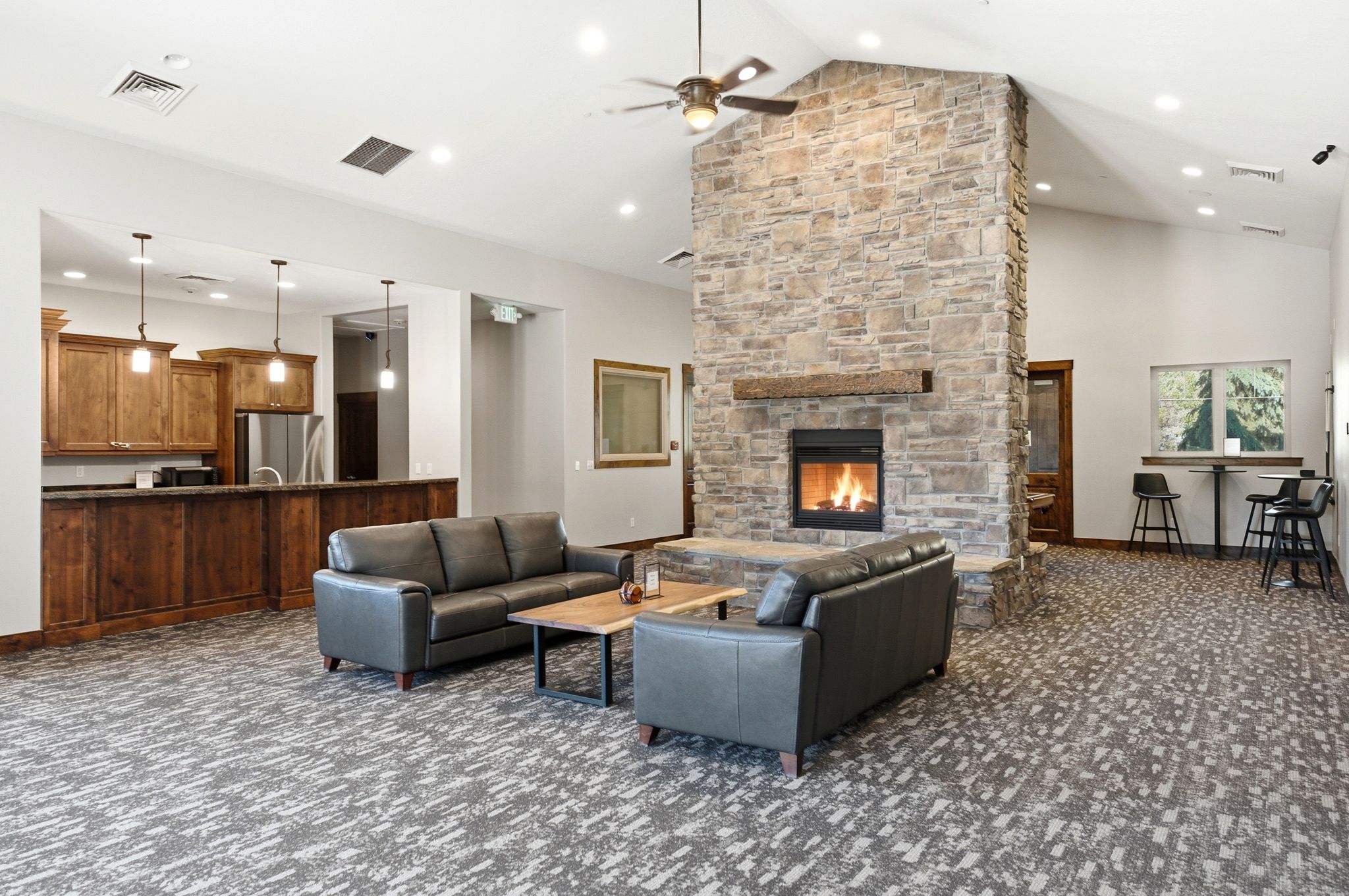 Spacious common area featuring a stone-clad fireplace with wood mantel, vaulted ceilings, and recessed lighting