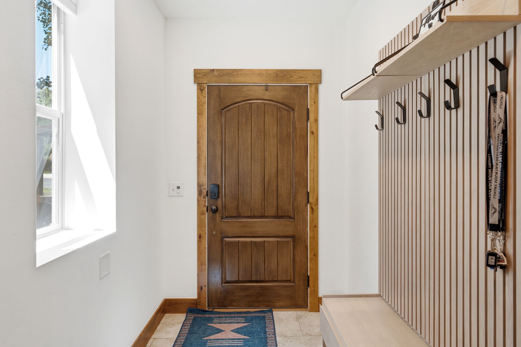 Entryway featuring a paneled wood door with a dark finish, wood-trim door casing, and a light wood-finish built-in bench with integrated hooks and a shelf