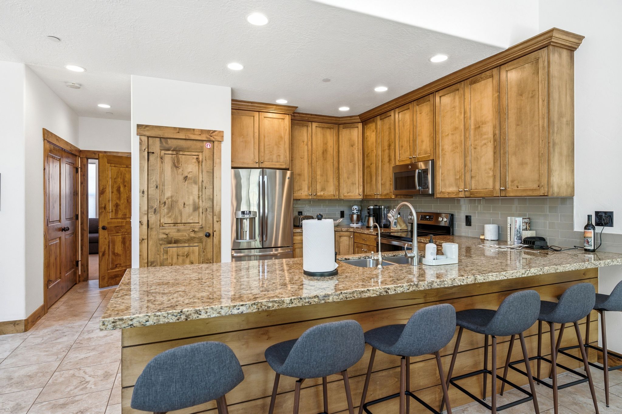 Kitchen featuring a large breakfast bar with stone countertop, stainless steel appliances, wood-finish cabinetry, a subway tile backsplash, and recessed lighting