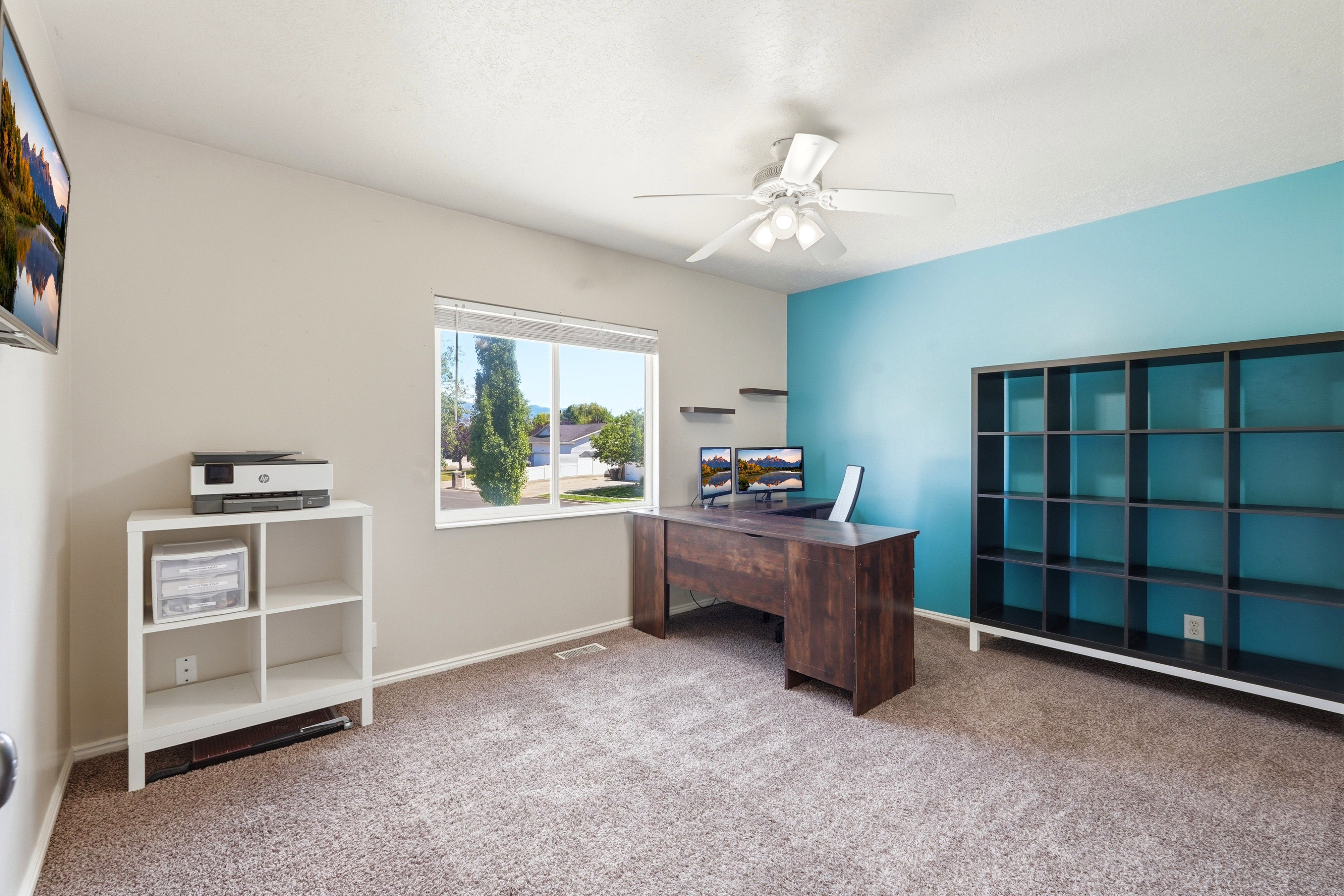Spacious room featuring carpeting, a prominent window, ceiling fan with light fixture, and a built-in shelving unit