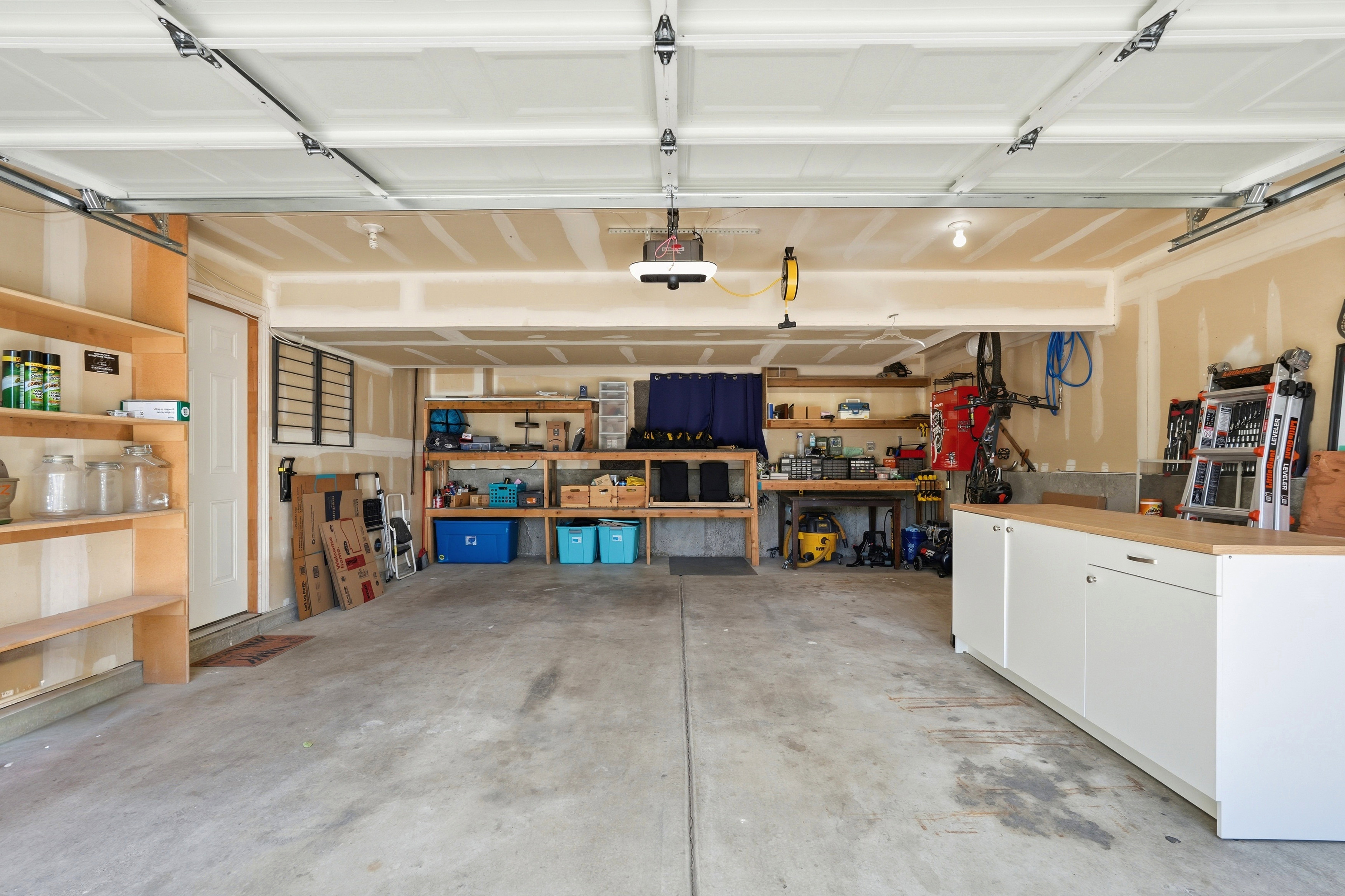 Spacious garage featuring a concrete floor, overhead garage door, built-in wooden shelving, and additional white cabinetry with a wood-finish countertop