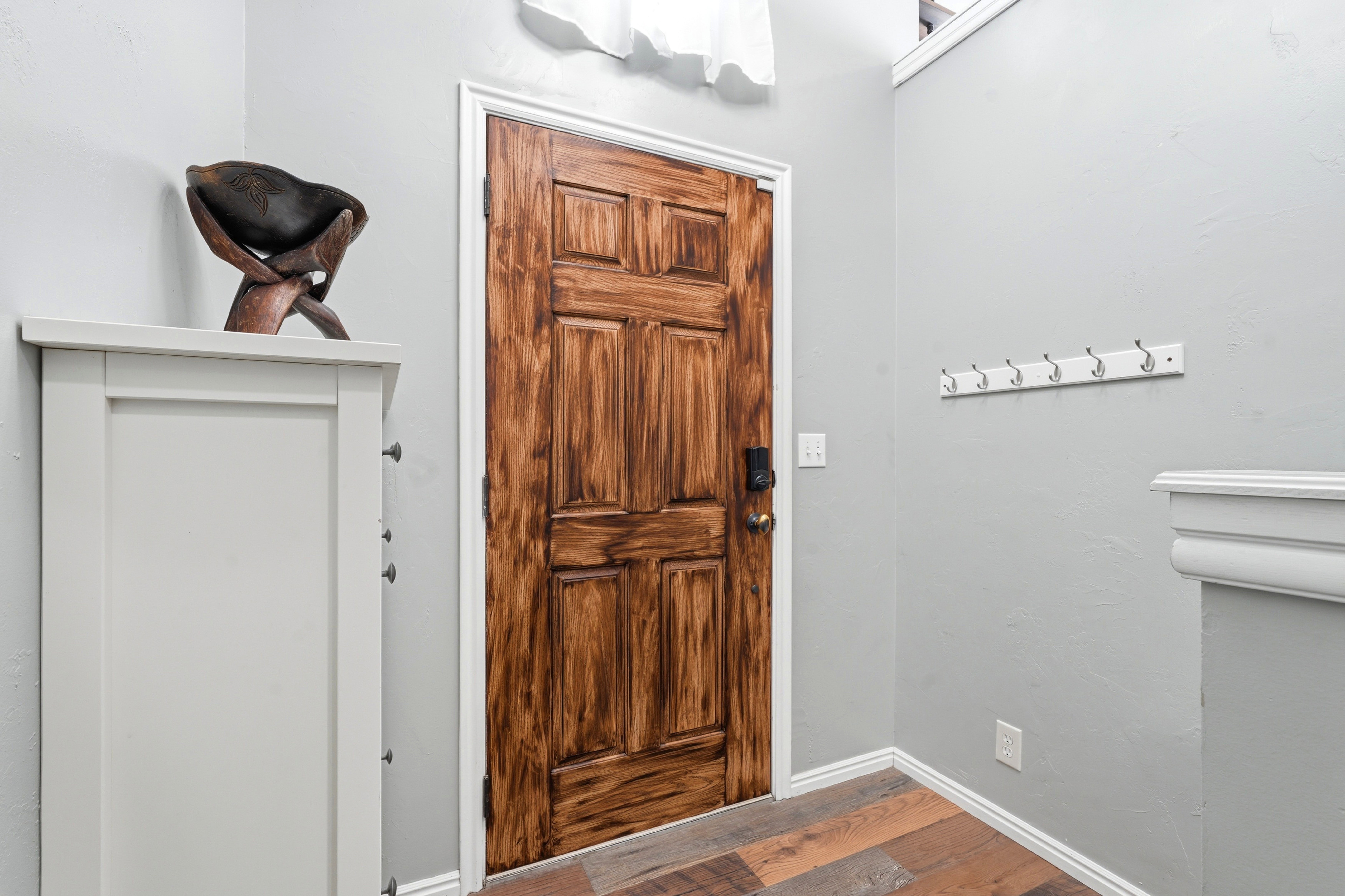 Paneled wood entry door with dark hardware, light gray walls, white baseboards, and wood-finish flooring