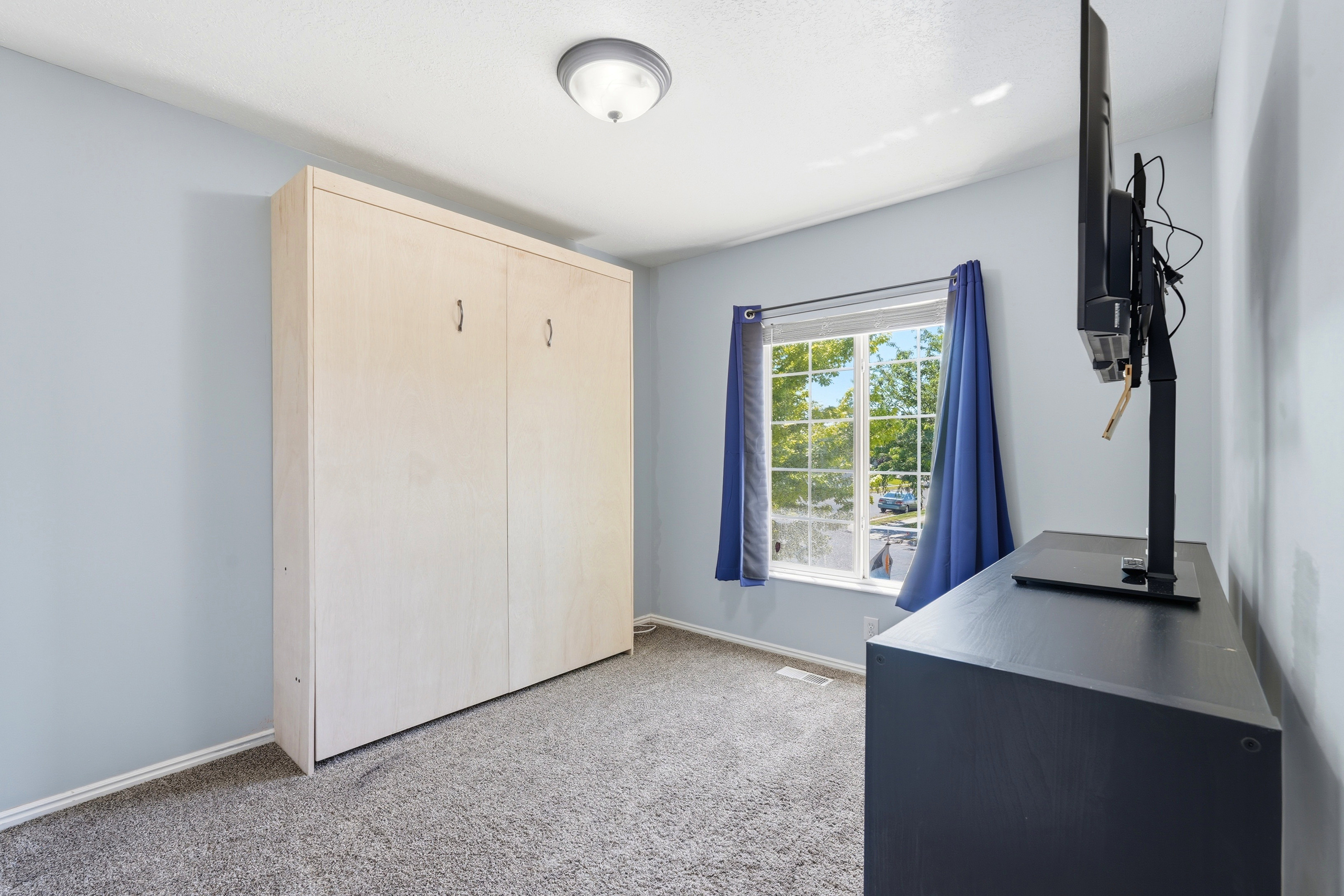 Room featuring a light-toned wood-finish built-in wall unit, a window with exterior visibility, and a gray carpeted floor