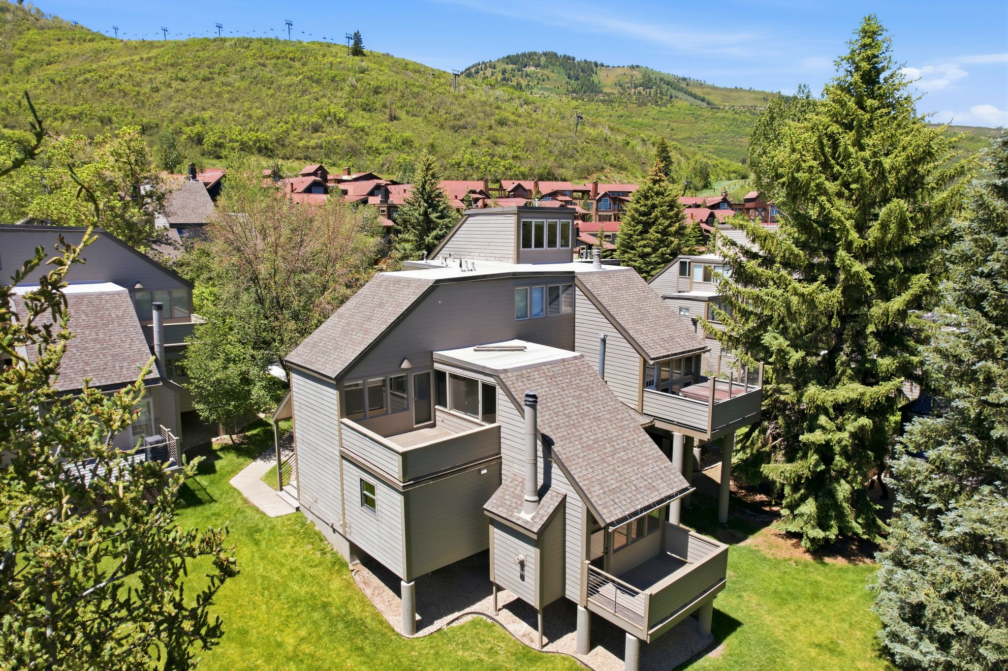Multi-level residence featuring gray siding, multiple private balconies with railings, sloped shingle roofing, and established surrounding greenery