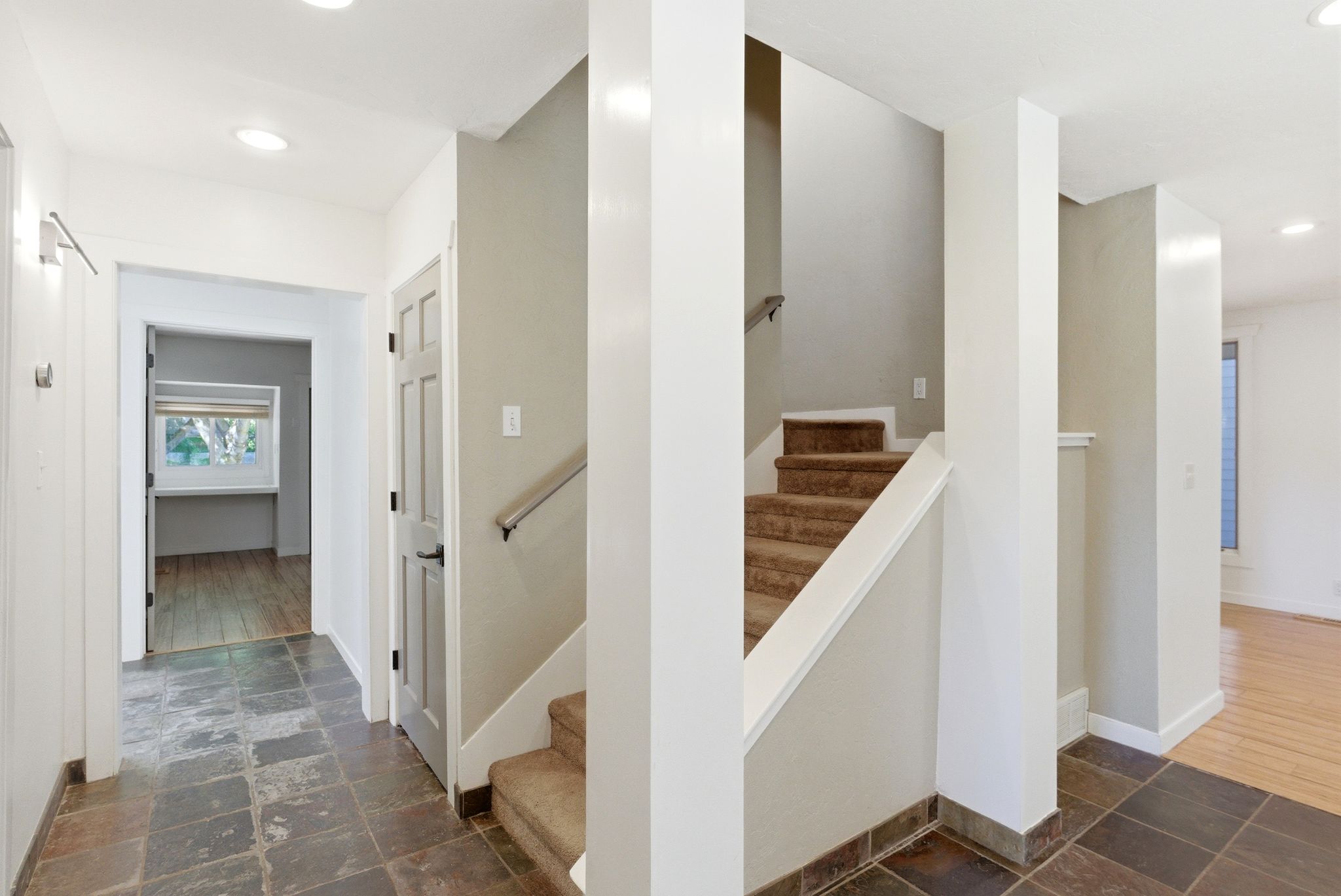 Entryway featuring stone-look tile flooring, recessed lighting, a carpeted staircase with a metal handrail, and a paneled interior door with black hardware