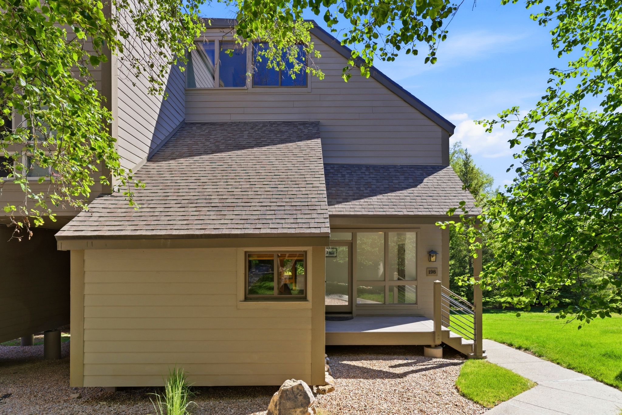 Multi-level exterior with neutral siding, a covered entrance, contemporary railings, and an asphalt shingle roof
