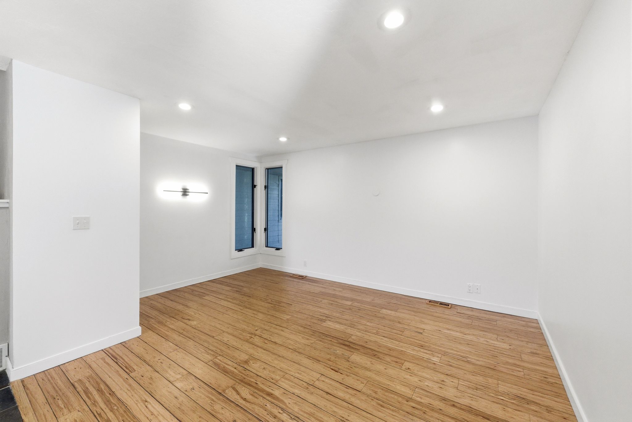 Spacious room featuring wood-finish flooring, recessed lighting, and a modern wall sconce
