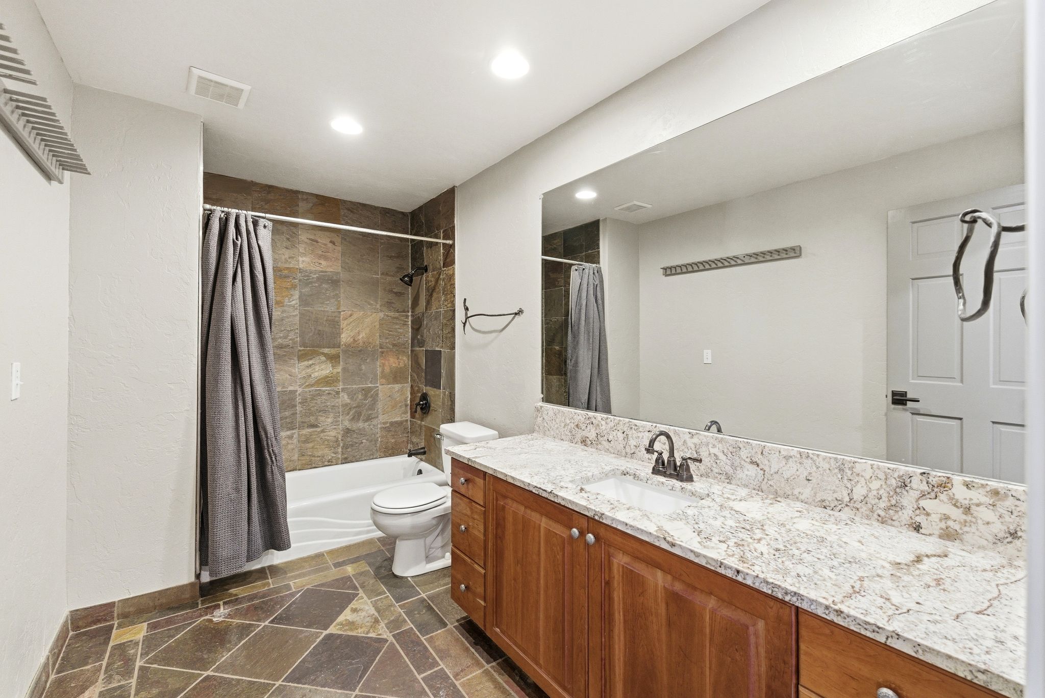 Bathroom featuring a long vanity with wood cabinetry and a stone countertop, a large wall-mounted mirror, a tiled shower-tub combination, and tiled flooring