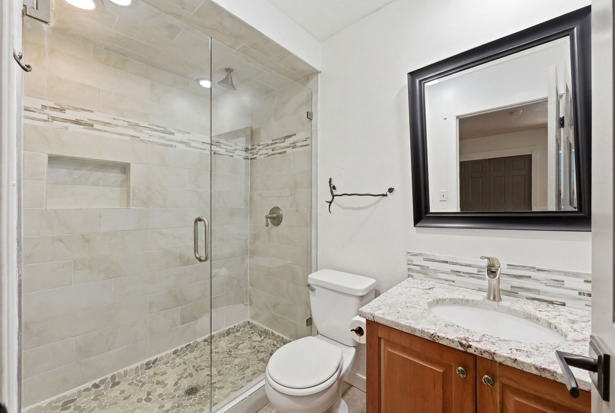 Shower enclosure featuring a glass door, pebble floor, and tiled walls with a decorative accent band and recessed niche