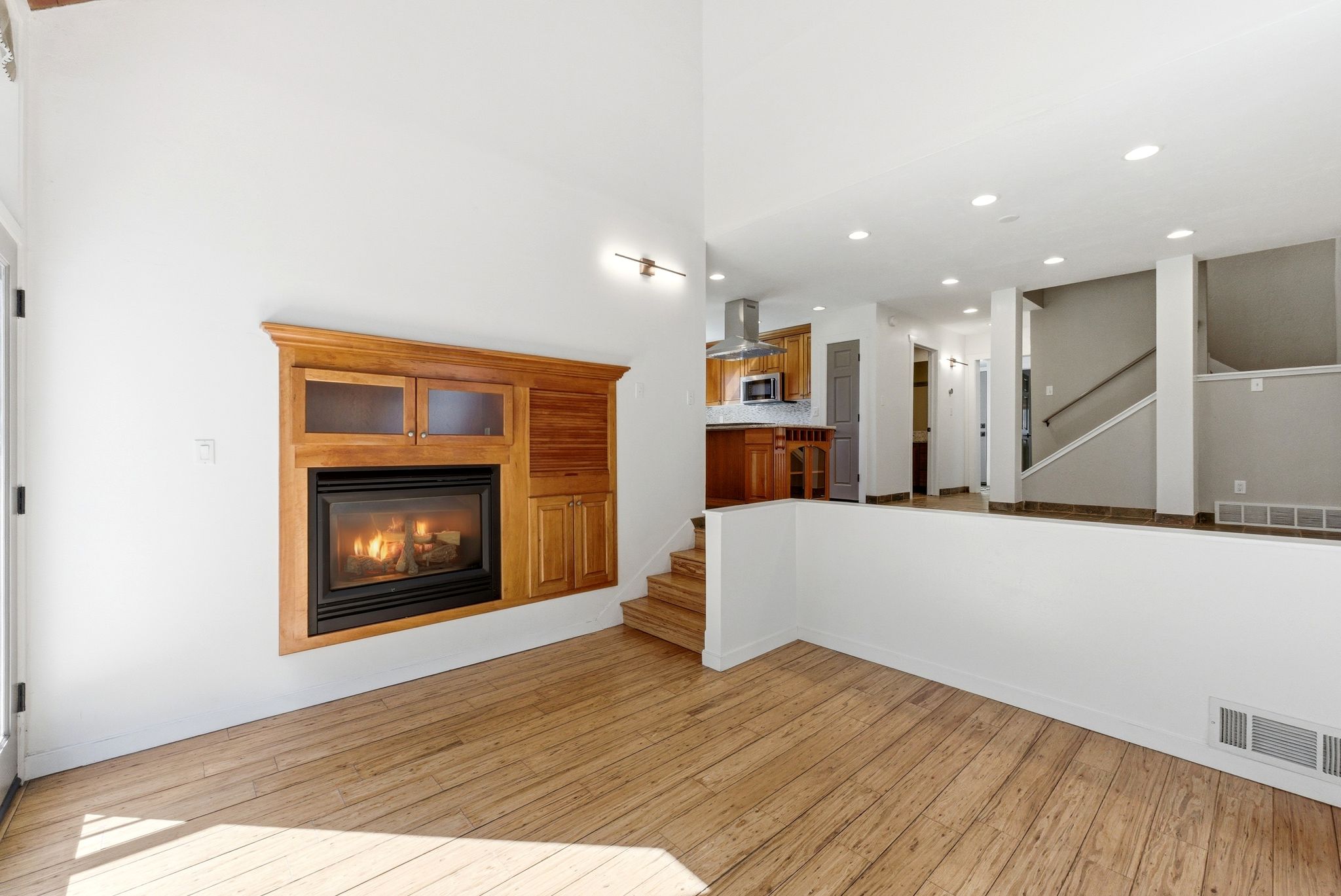 Living area featuring a fireplace with built-in wood cabinetry, wood-finish flooring, recessed lighting, and a partial wall separating spaces