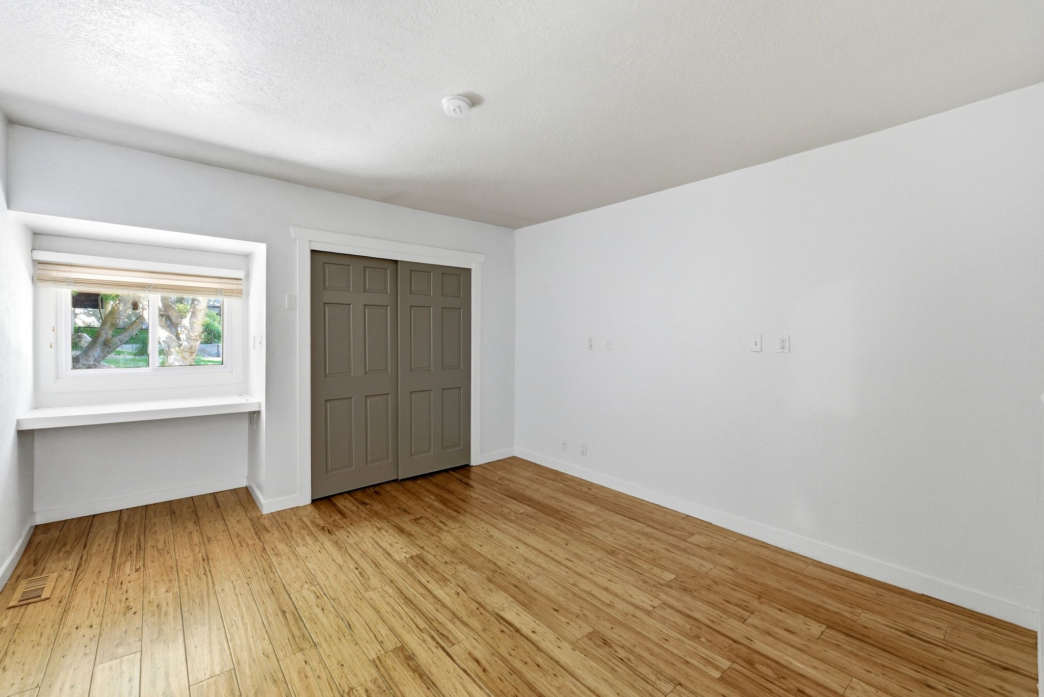 Room featuring wood-finish flooring, a window with a built-in sill and wood blinds, and a closet with paneled bi-fold doors