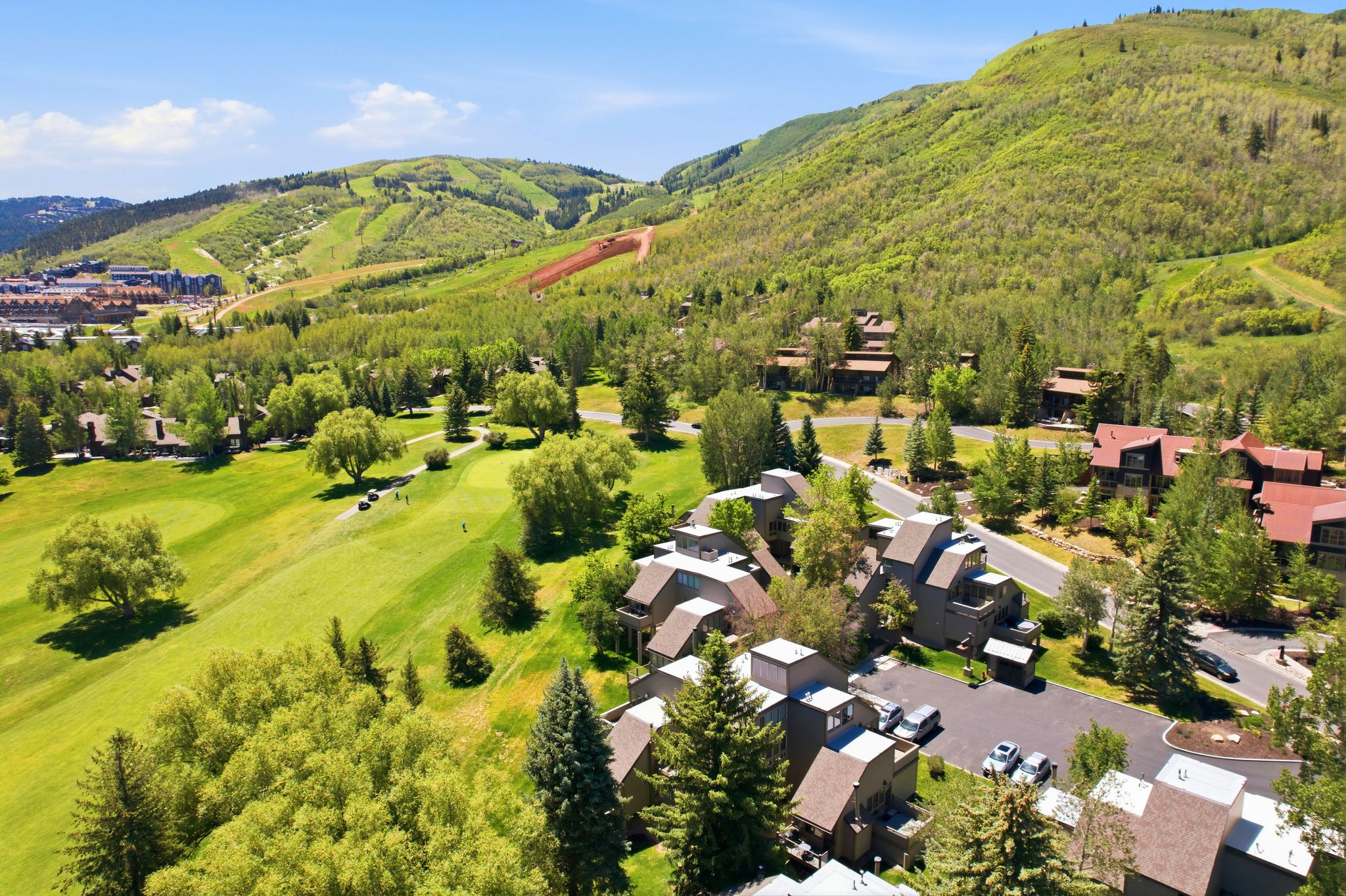 Mountain community featuring multi-story residences, paved roadways, mature evergreen trees, and a manicured golf course