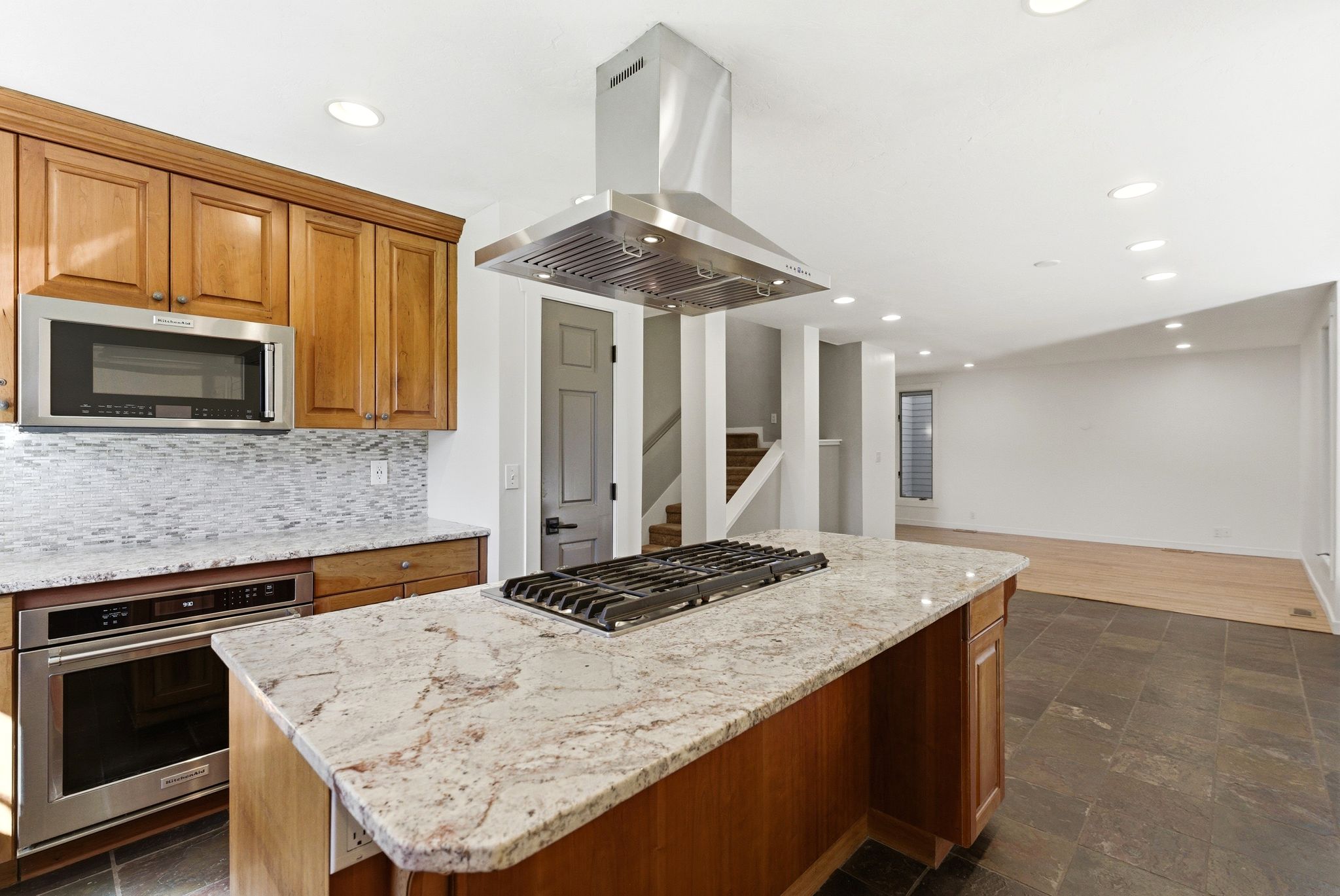 Kitchen island with a built-in gas cooktop, granite countertop, and stainless steel range hood