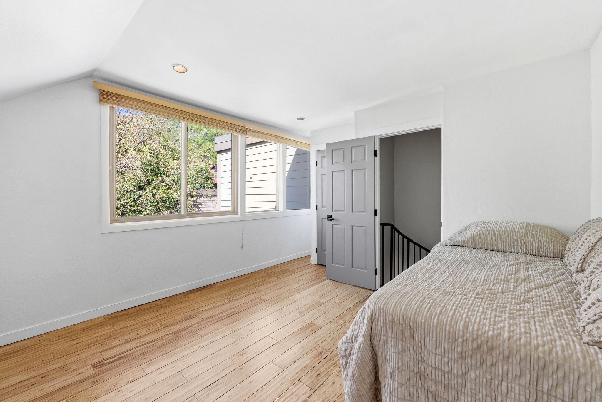 Bright room featuring multiple windows with natural wood blinds, light wood-finish flooring, recessed lighting, and a paneled interior door