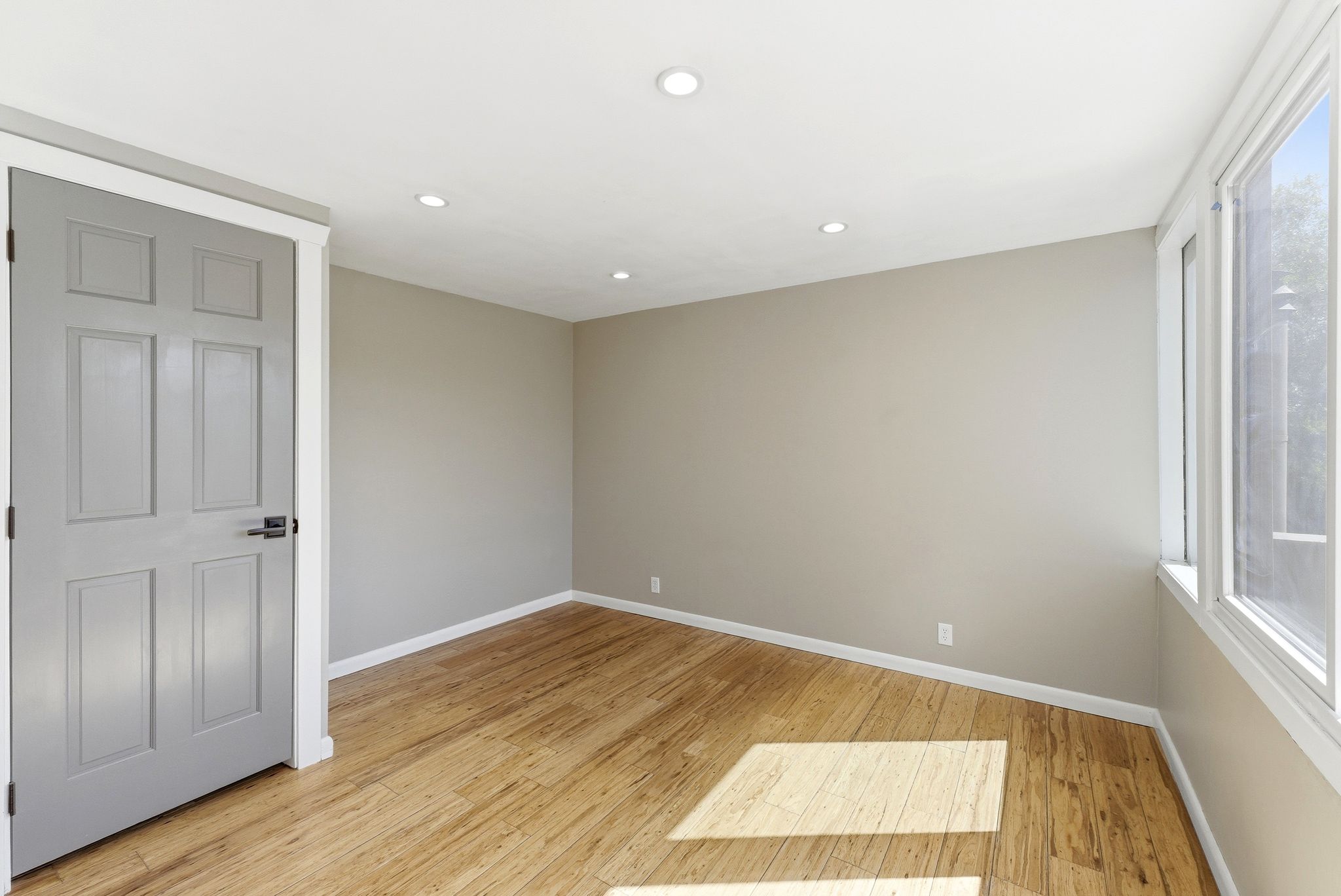 Bright interior room featuring wood-finish flooring, recessed ceiling lighting, a multi-pane window, neutral wall tones, and white trim