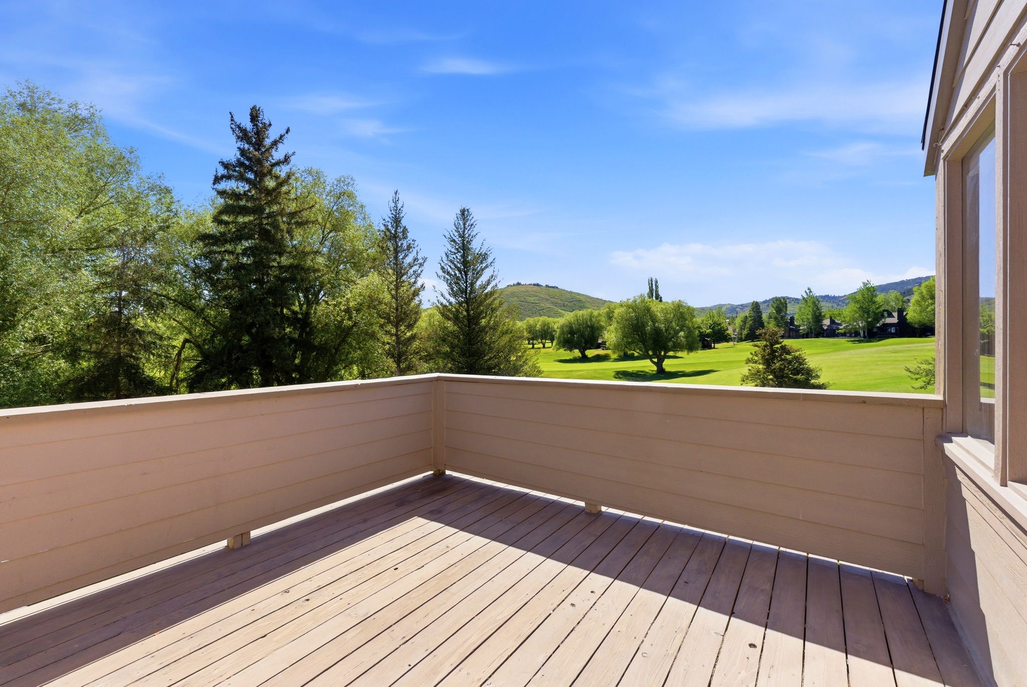 Expansive outdoor deck with natural wood-finish flooring and a neutral-toned privacy wall