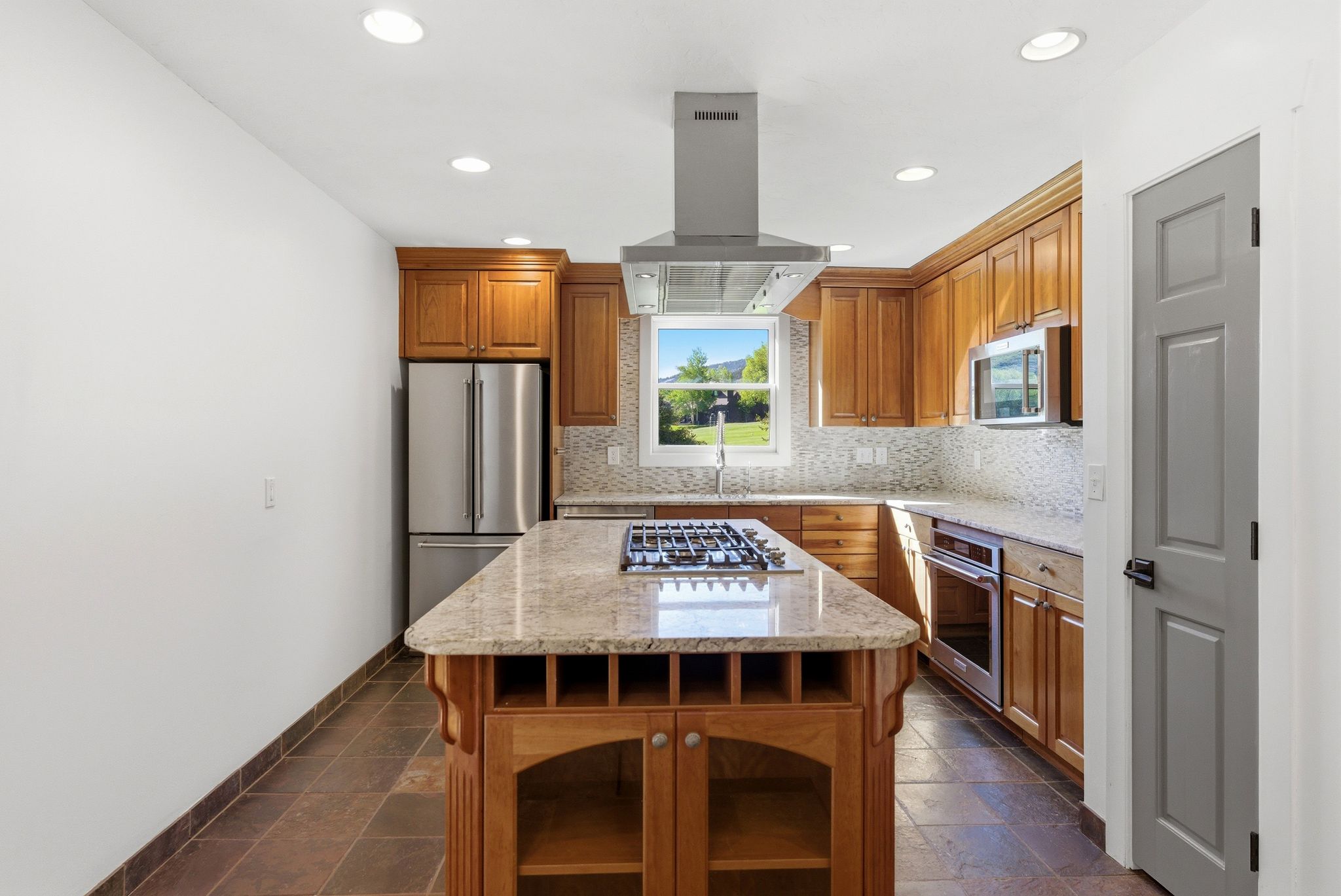 Kitchen featuring a central island with a gas cooktop, granite-style countertops, wood cabinetry, stainless steel appliances, and tile flooring
