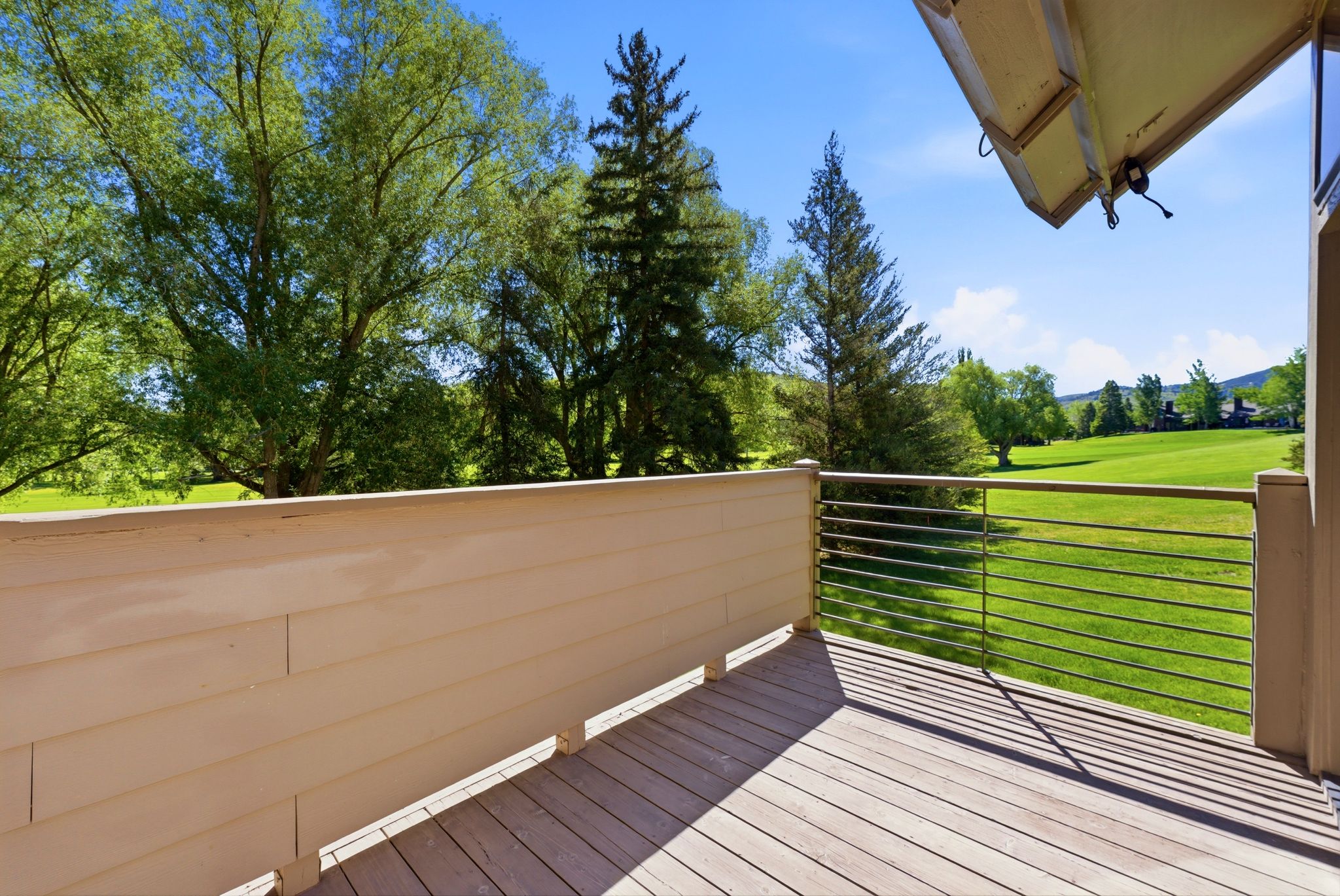 Outdoor deck featuring wood-finish flooring, a horizontal cable railing system, and a scenic green landscape with mature trees