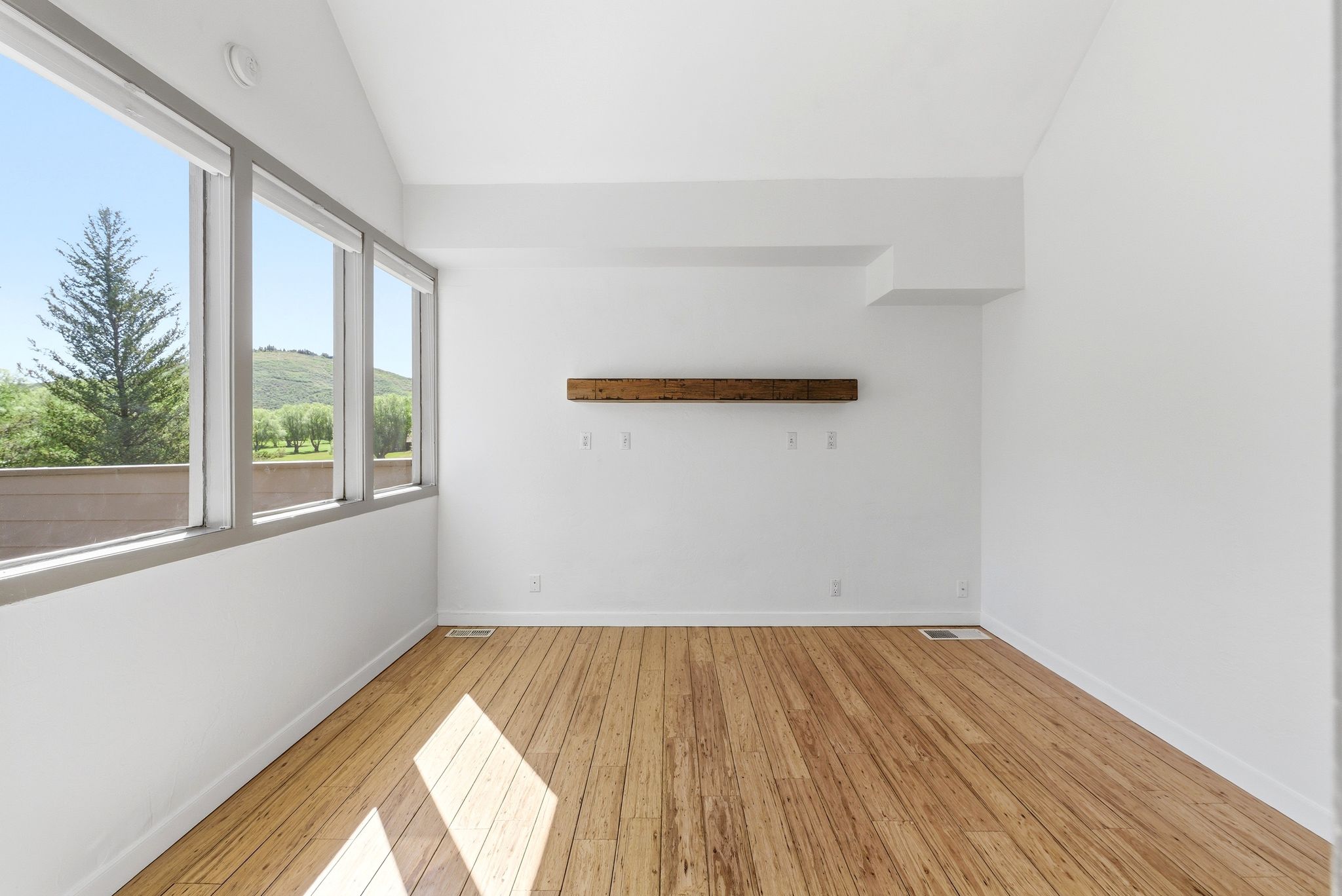 Room featuring wood-finish flooring, a vaulted ceiling, a built-in wood shelf, and multiple large windows overlooking a natural landscape