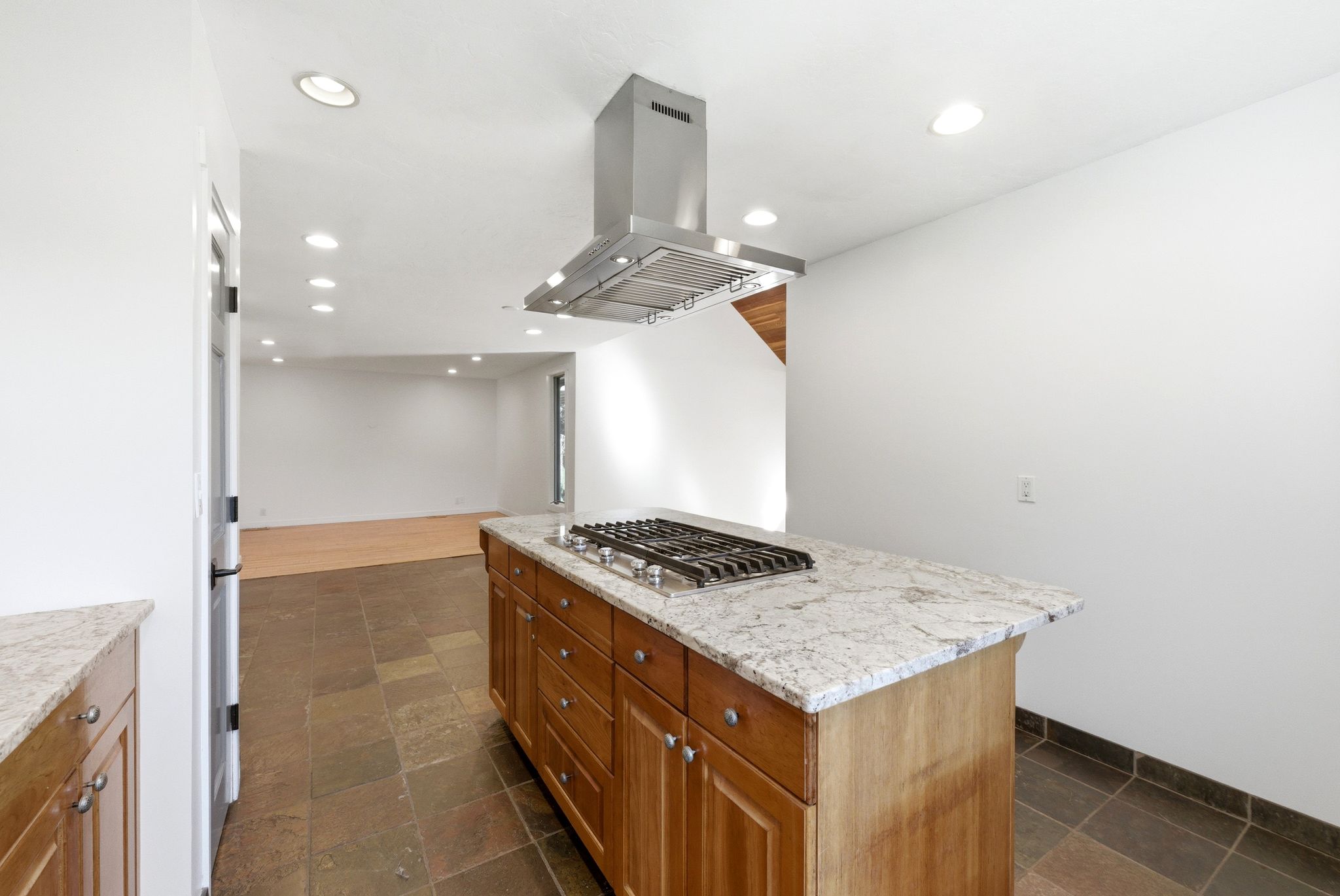 Kitchen island featuring a gas cooktop, granite countertop, wood cabinetry, and stainless steel range hood