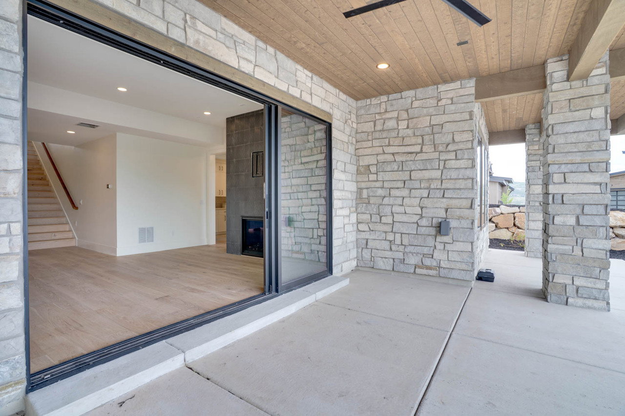 Expansive outdoor living area featuring a stone accent wall, wood-finish ceiling, and concrete patio