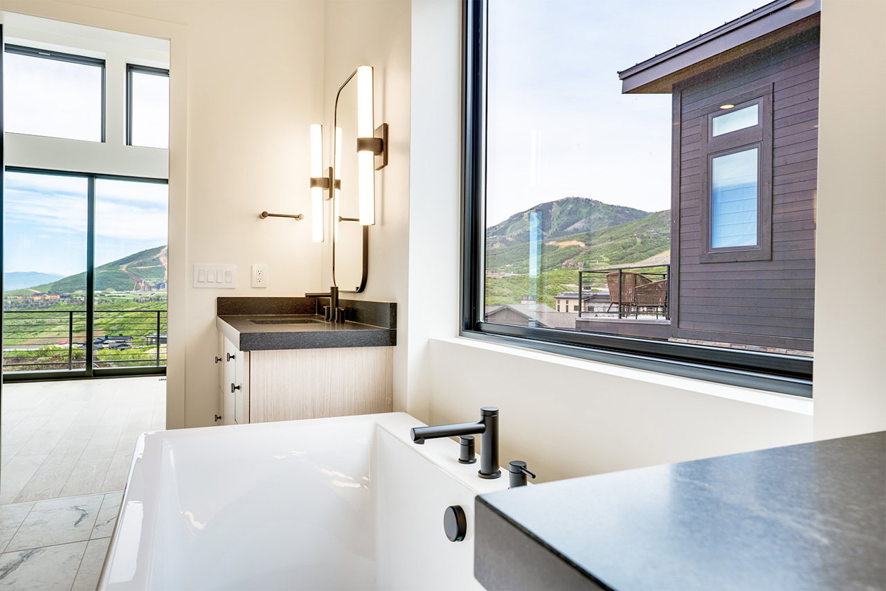 Freestanding soaking tub with a wall-mounted faucet, complemented by a vanity featuring a dark countertop, integrated sink, and contemporary lighting fixtures