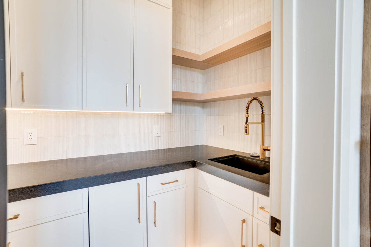White cabinetry featuring sleek gold-tone hardware, dark countertops, and a black sink with a gold-tone faucet
