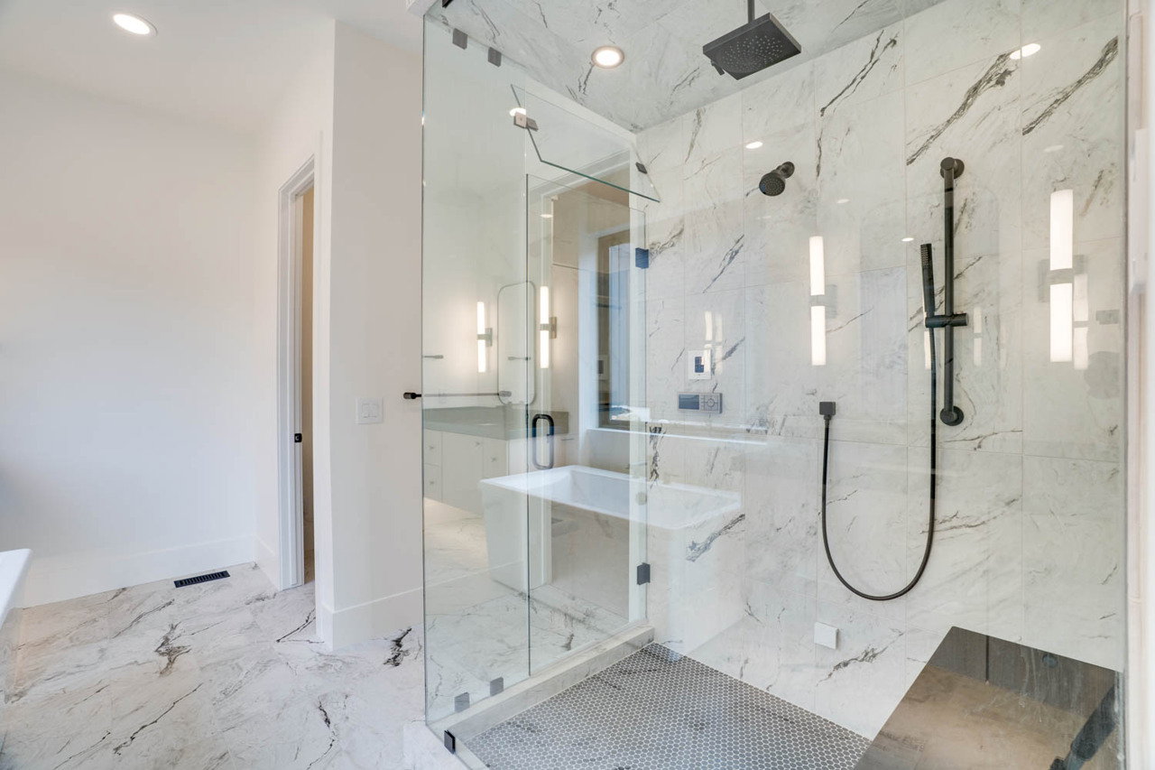 Glass-enclosed shower with a rainfall showerhead, handheld shower, and integrated seating