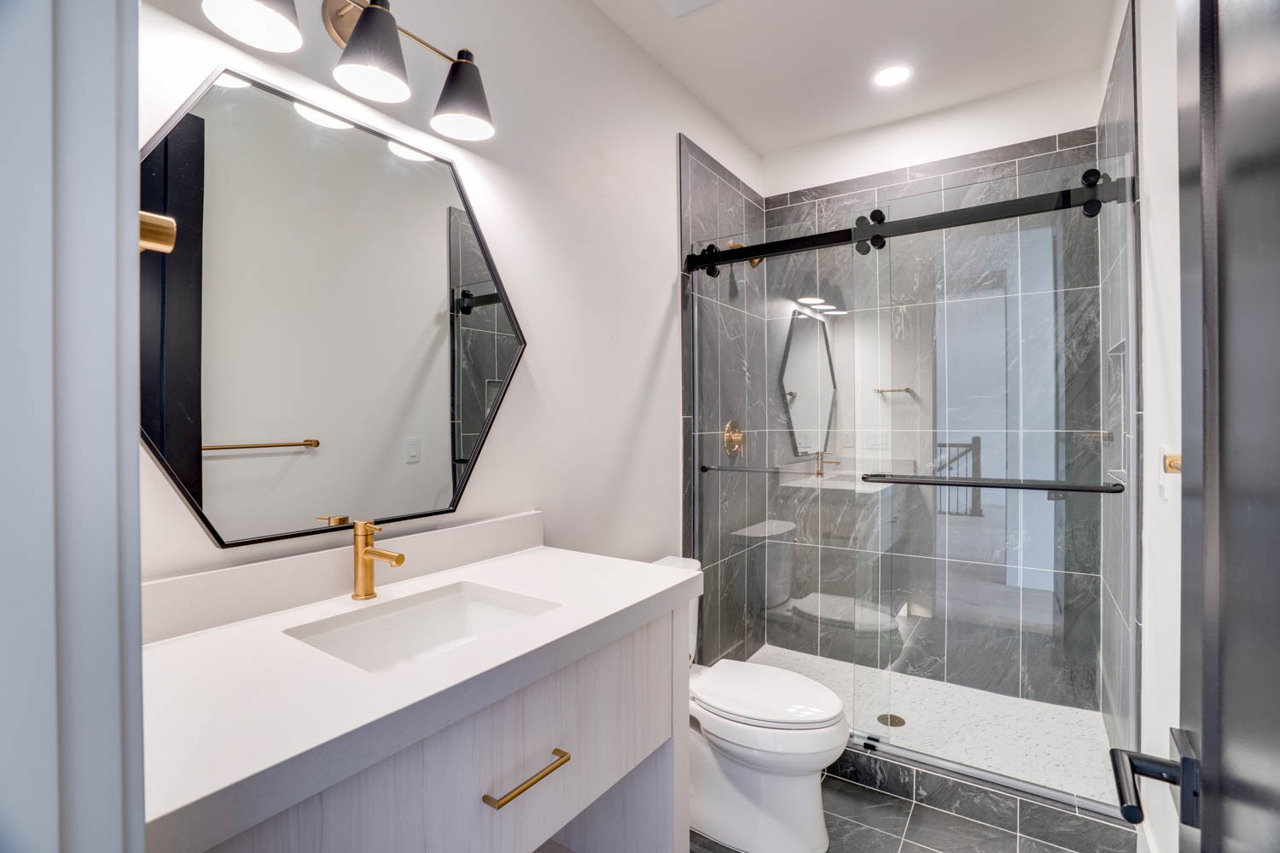 Contemporary bathroom featuring a white vanity with integrated sink, gold-finish faucet, and an octagonal mirror