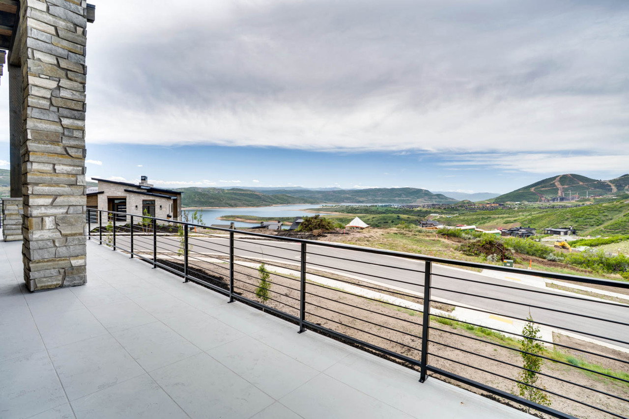 Exterior balcony featuring a stone-clad pillar, horizontal metal railing, and light-toned flooring