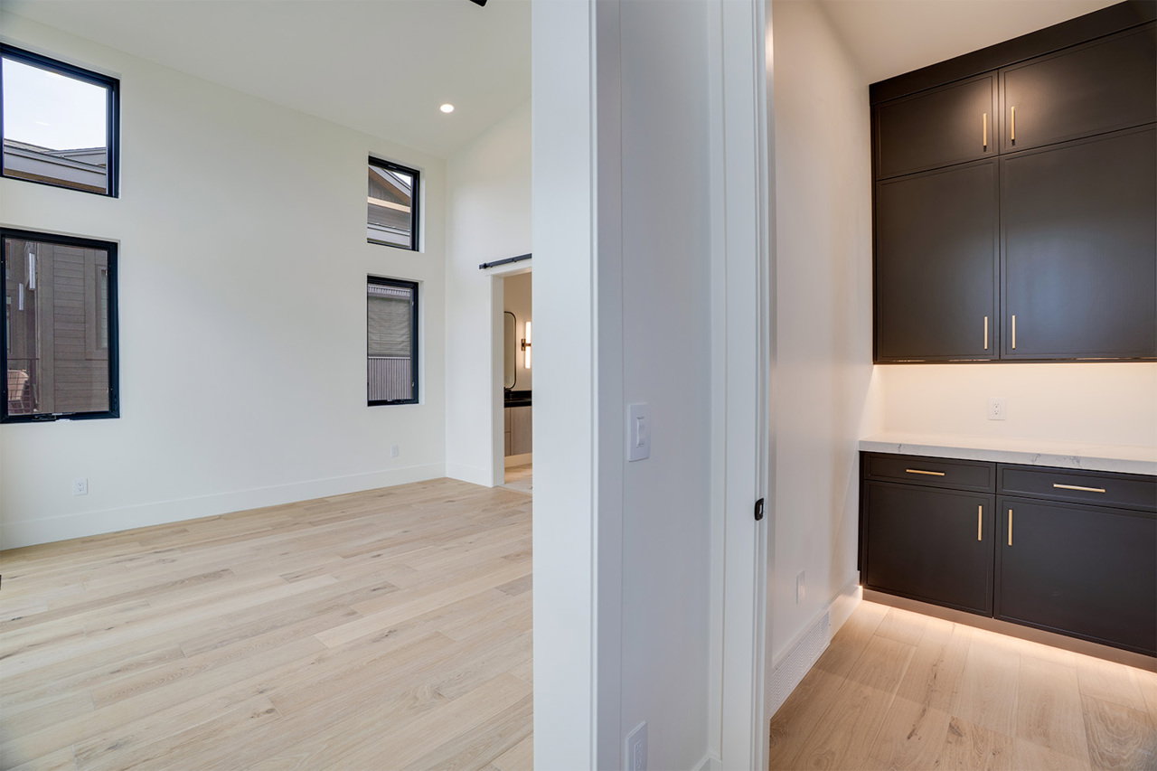 Spacious room with light wood-finish flooring, high ceilings, and multiple windows with black frames
