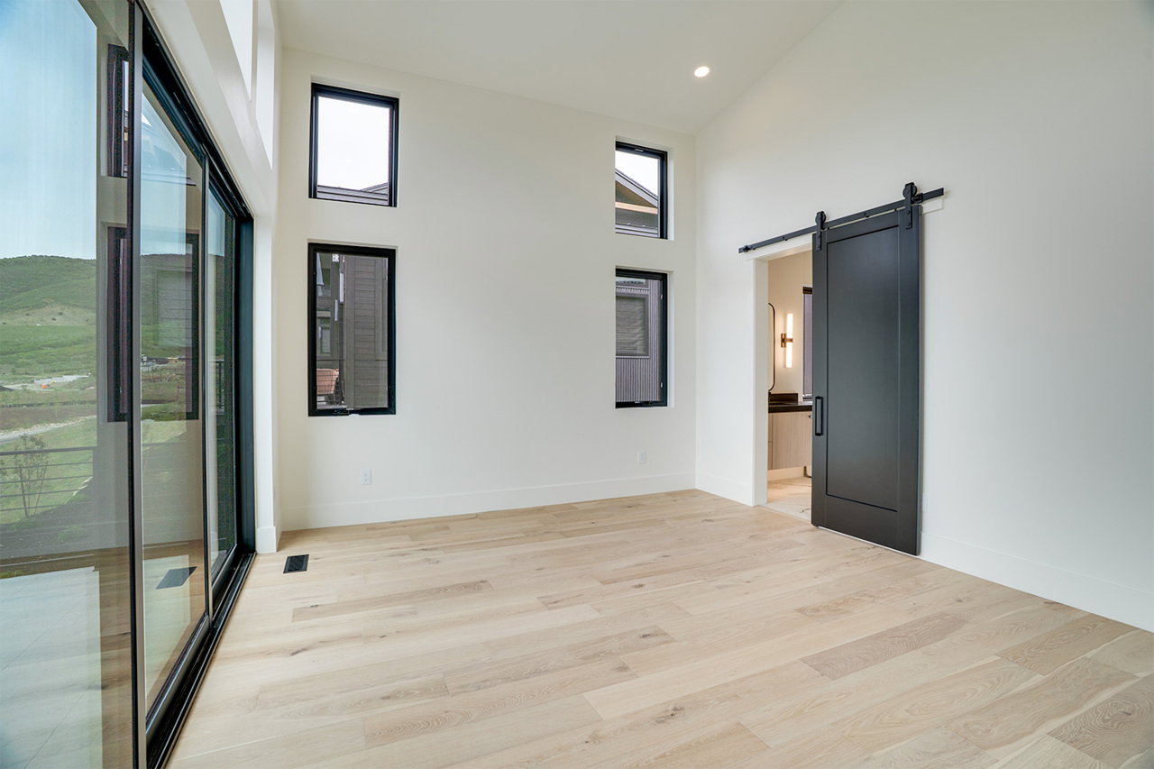 Spacious room featuring light wood-finish flooring, vaulted ceilings, and a large sliding glass door