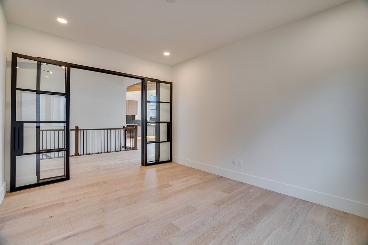 Spacious room featuring light wood-finish flooring, recessed lighting, and modern black-framed glass sliding doors
