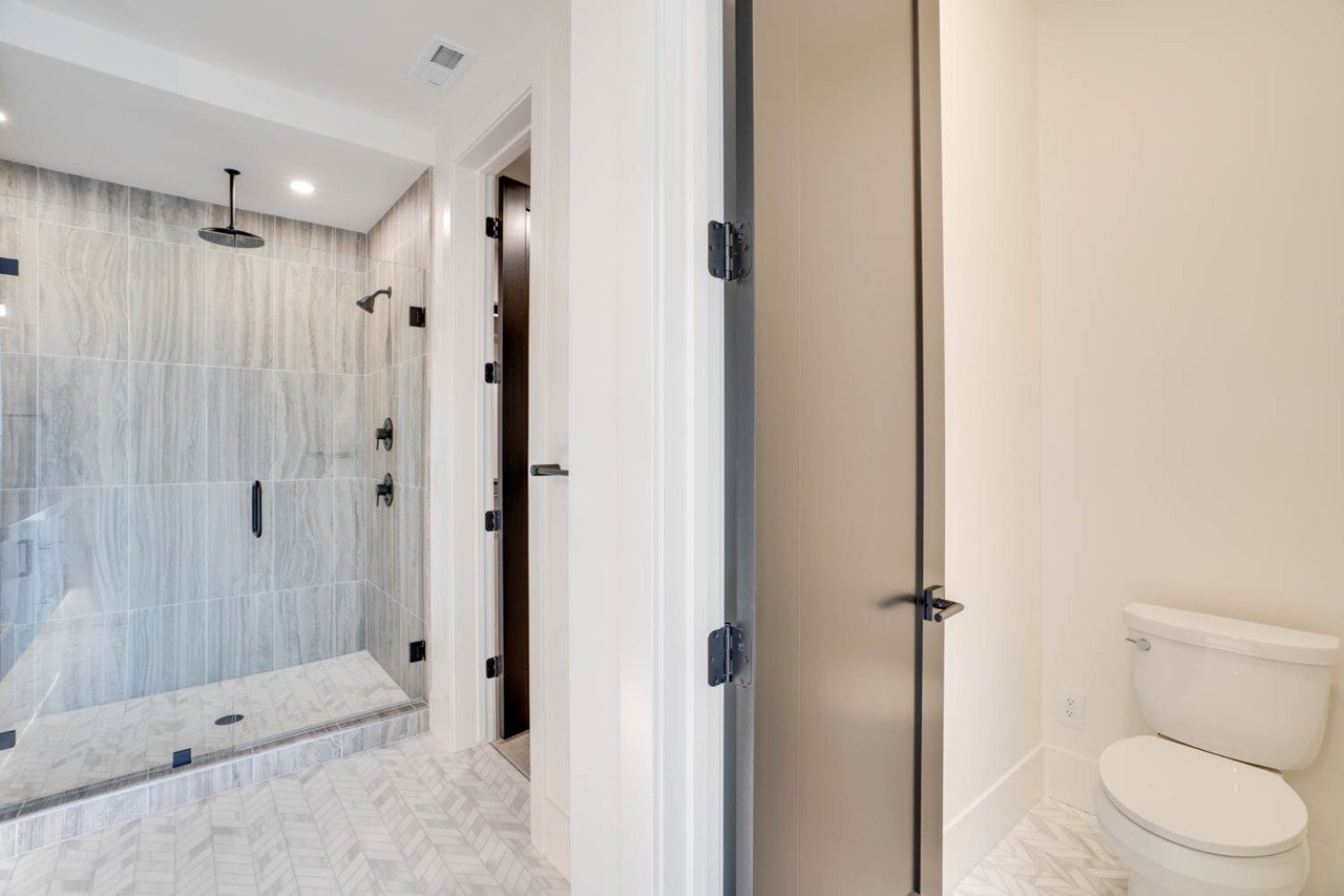 Spacious bathroom featuring a glass-enclosed shower with full-height tile surround, a ceiling-mounted rainfall showerhead, a wall-mounted showerhead, and matte black fixtures