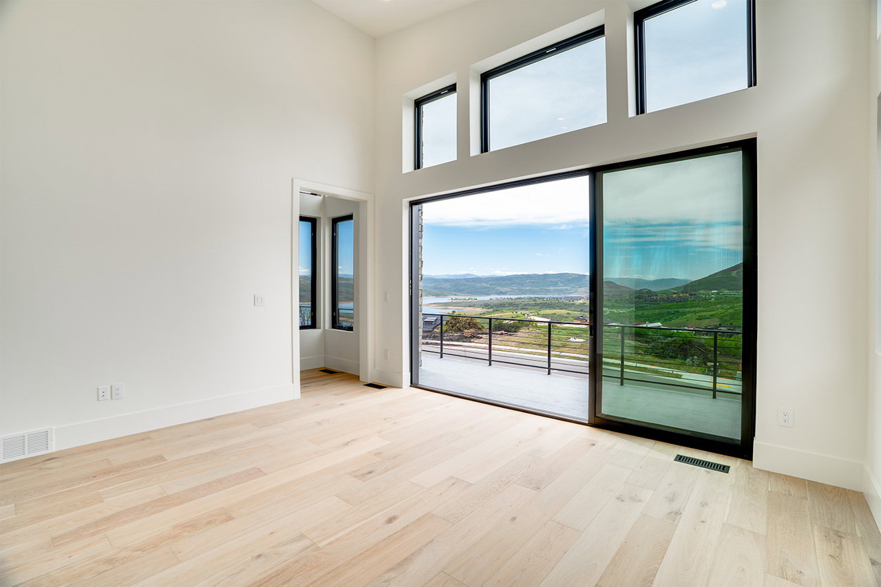 Spacious interior with light wood-finish flooring, high ceilings, and a sliding glass door opening to an outdoor balcony