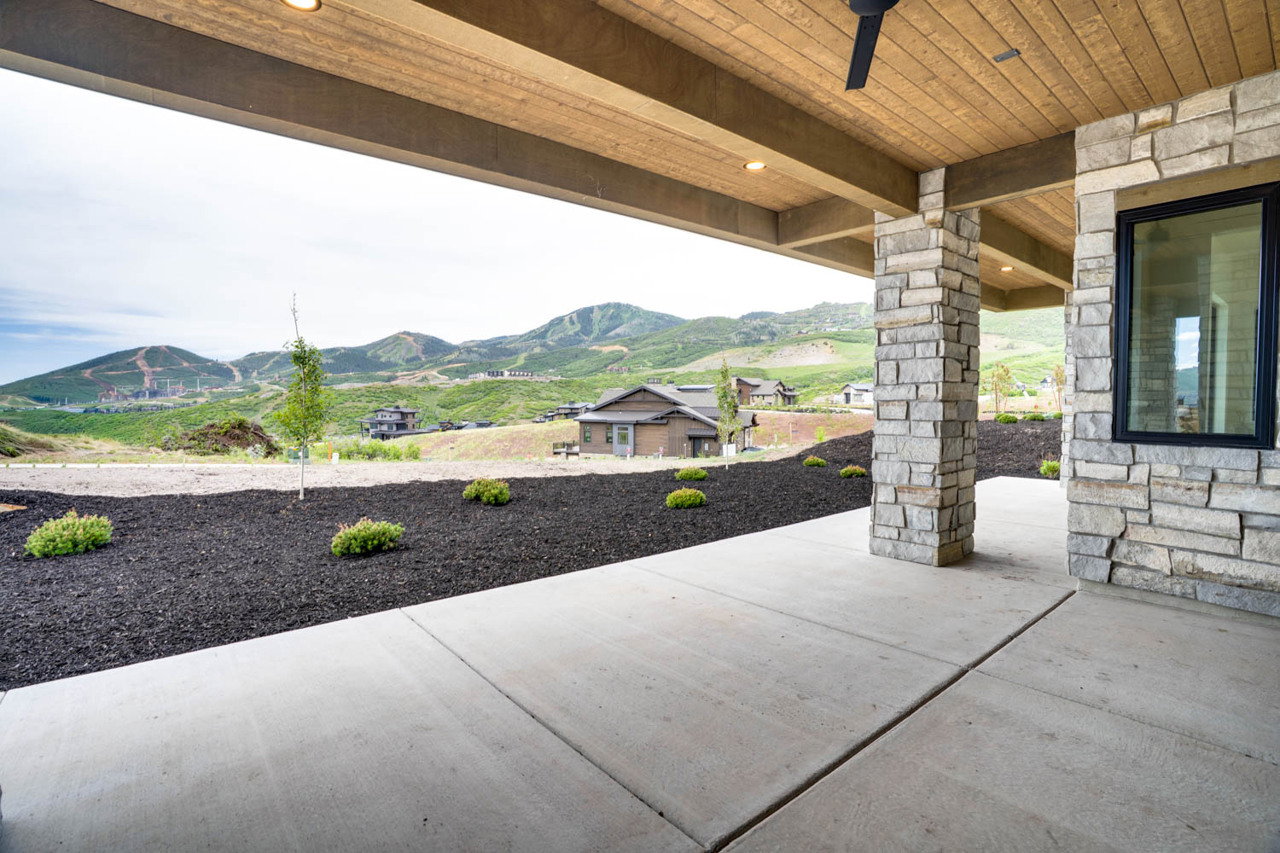 Covered patio with a concrete surface, stone-clad columns, and a wood-finish ceiling with recessed lighting