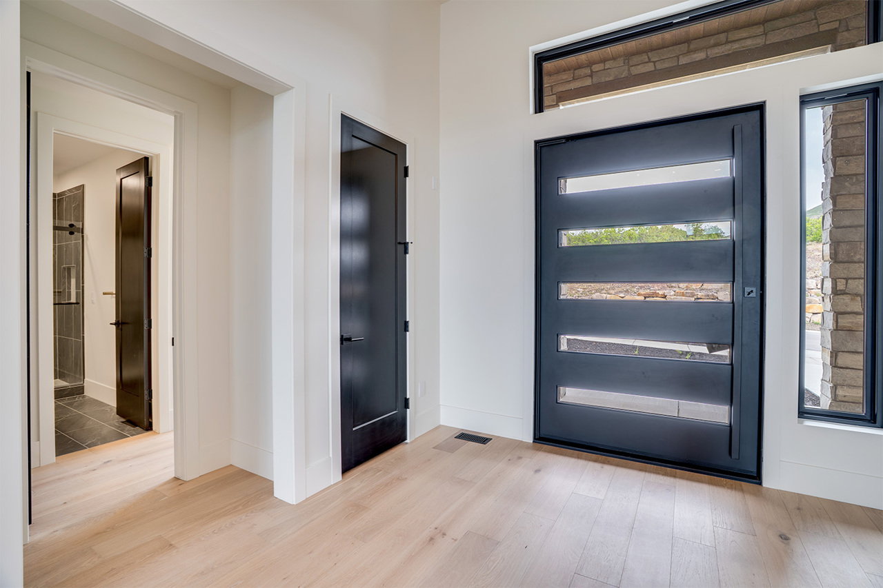 Modern entry featuring a dark-framed glass paneled door, coordinating transom window, and light wood-finish flooring