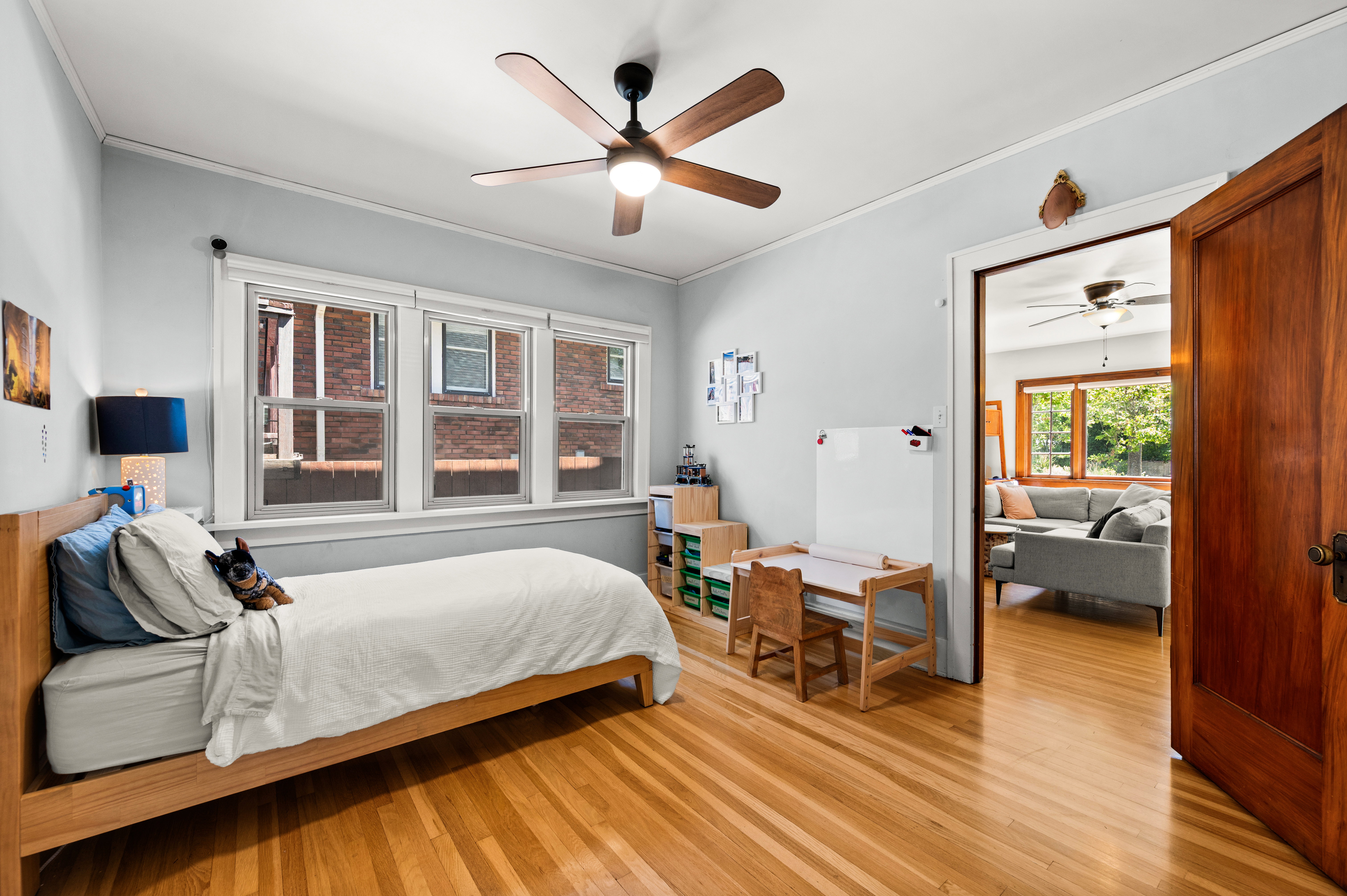 Hardwood flooring throughout, featuring a multi-pane window, ceiling fan with integrated lighting, and a solid wood door frame