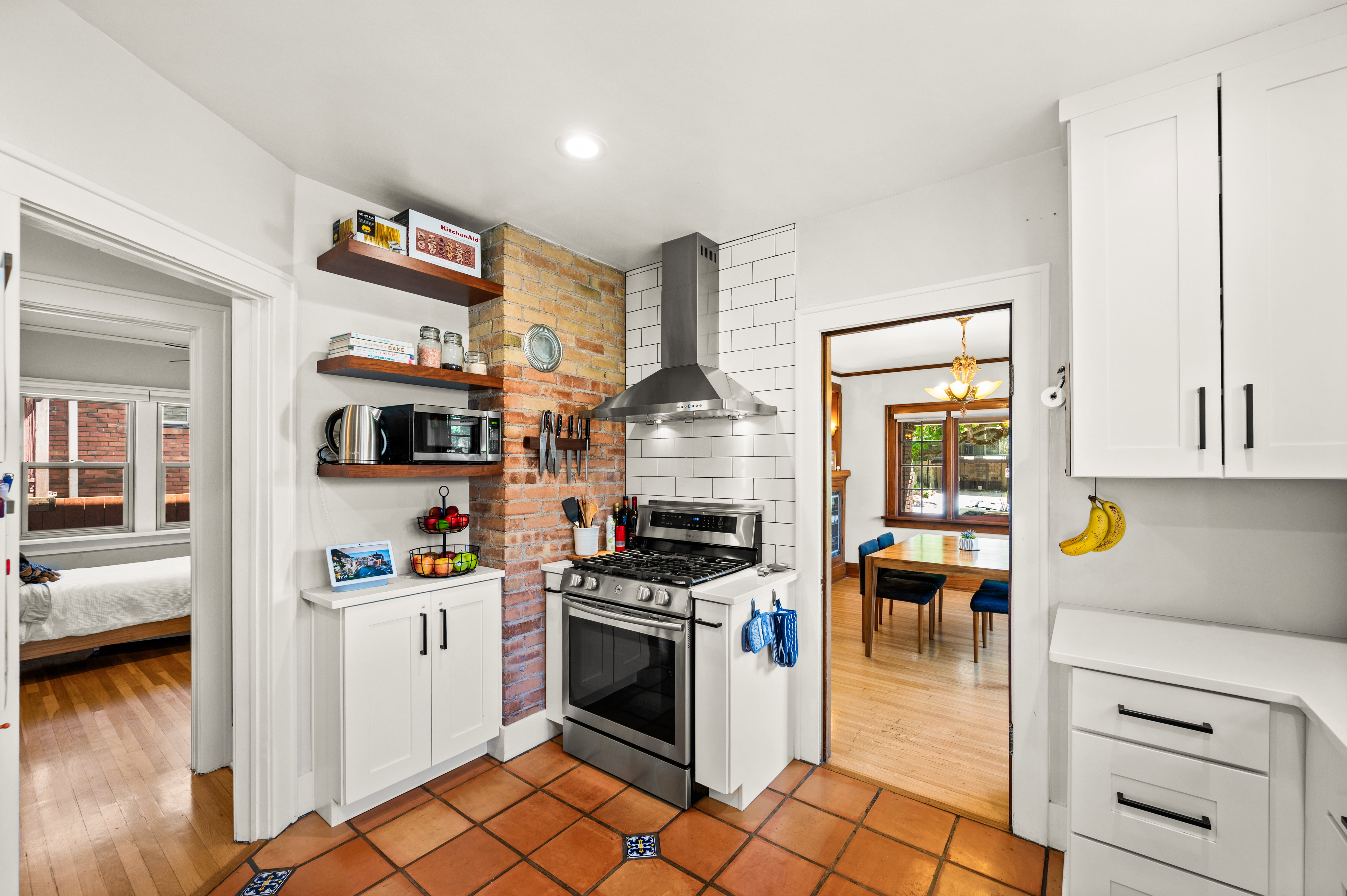 Kitchen featuring terracotta floor tiles with decorative accents, exposed brick backsplash, and stainless steel gas range with coordinating vent hood