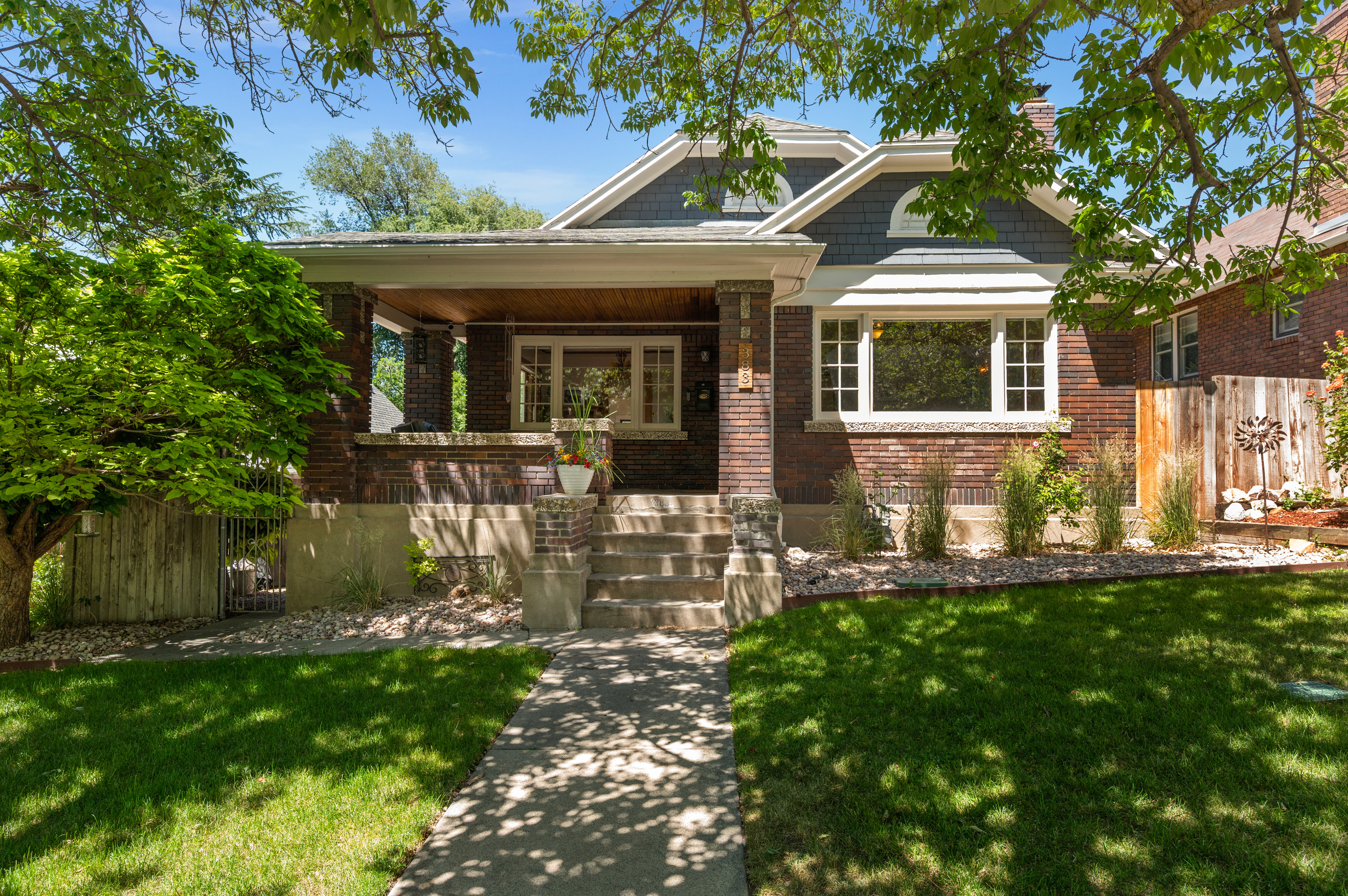 Traditional brick exterior featuring a covered front porch, a bay window with white trim, and a gabled roofline with shake siding