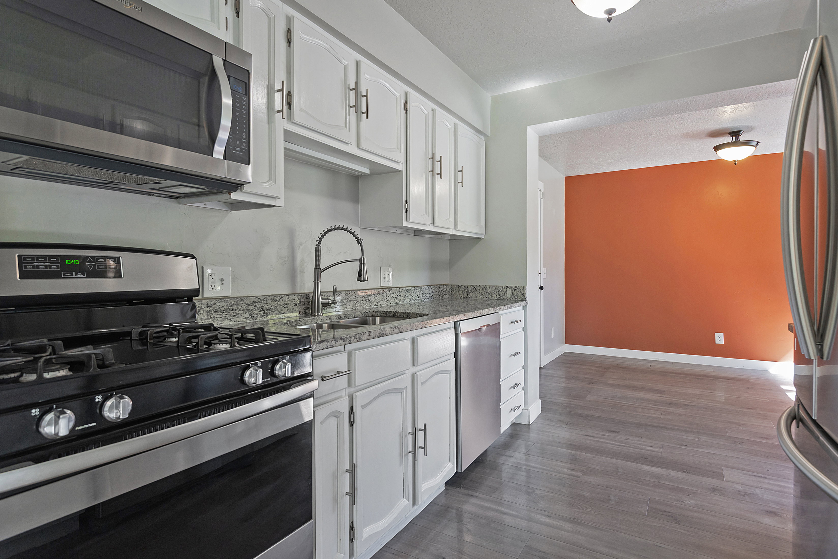 Kitchen featuring white cabinetry, granite countertops, and stainless steel appliances including an over-range microwave, gas range, and dishwasher