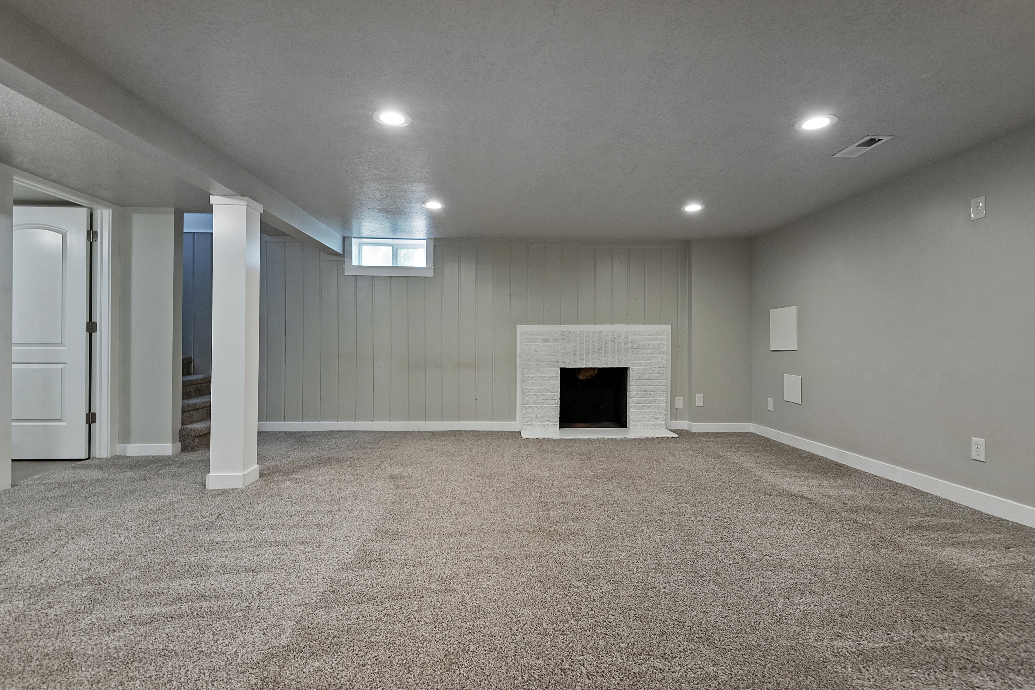 Spacious carpeted room featuring a white brick fireplace, recessed lighting, and a window with natural light