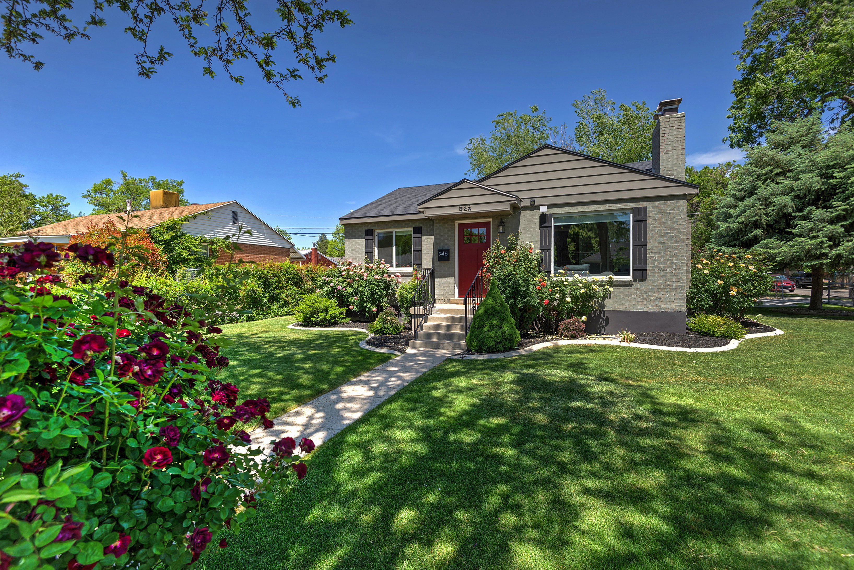 Charming single-story residence with a red entry door, framed by a manicured lawn and mature landscaping