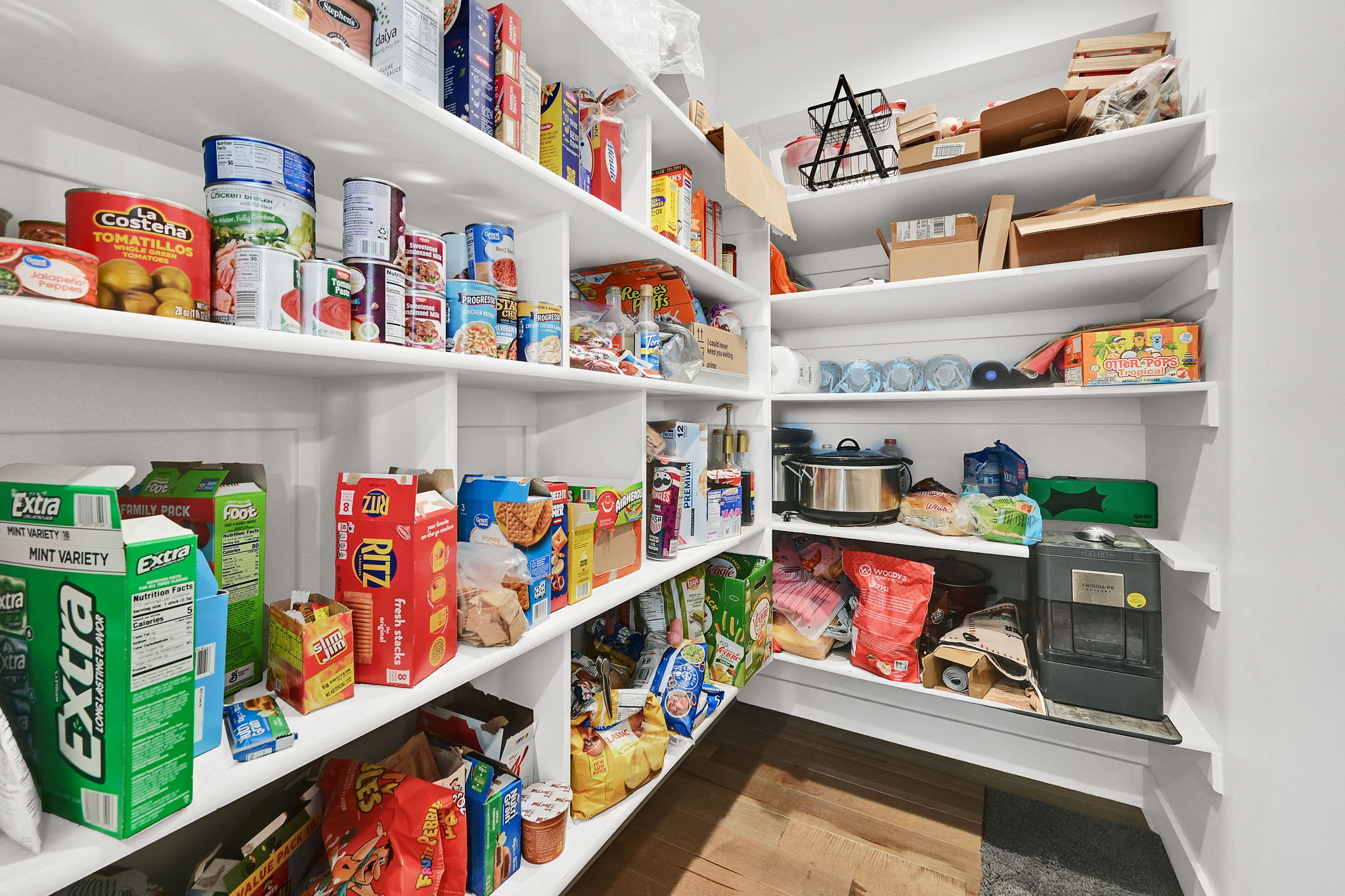 Built-in pantry with extensive white shelving, wood-finish flooring, and a corner configuration maximizing storage capacity