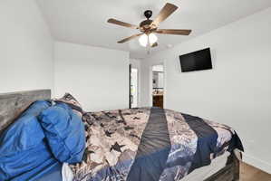 Bright bedroom featuring a ceiling fan with integrated lighting, wood-finish flooring, and a wall-mounted television