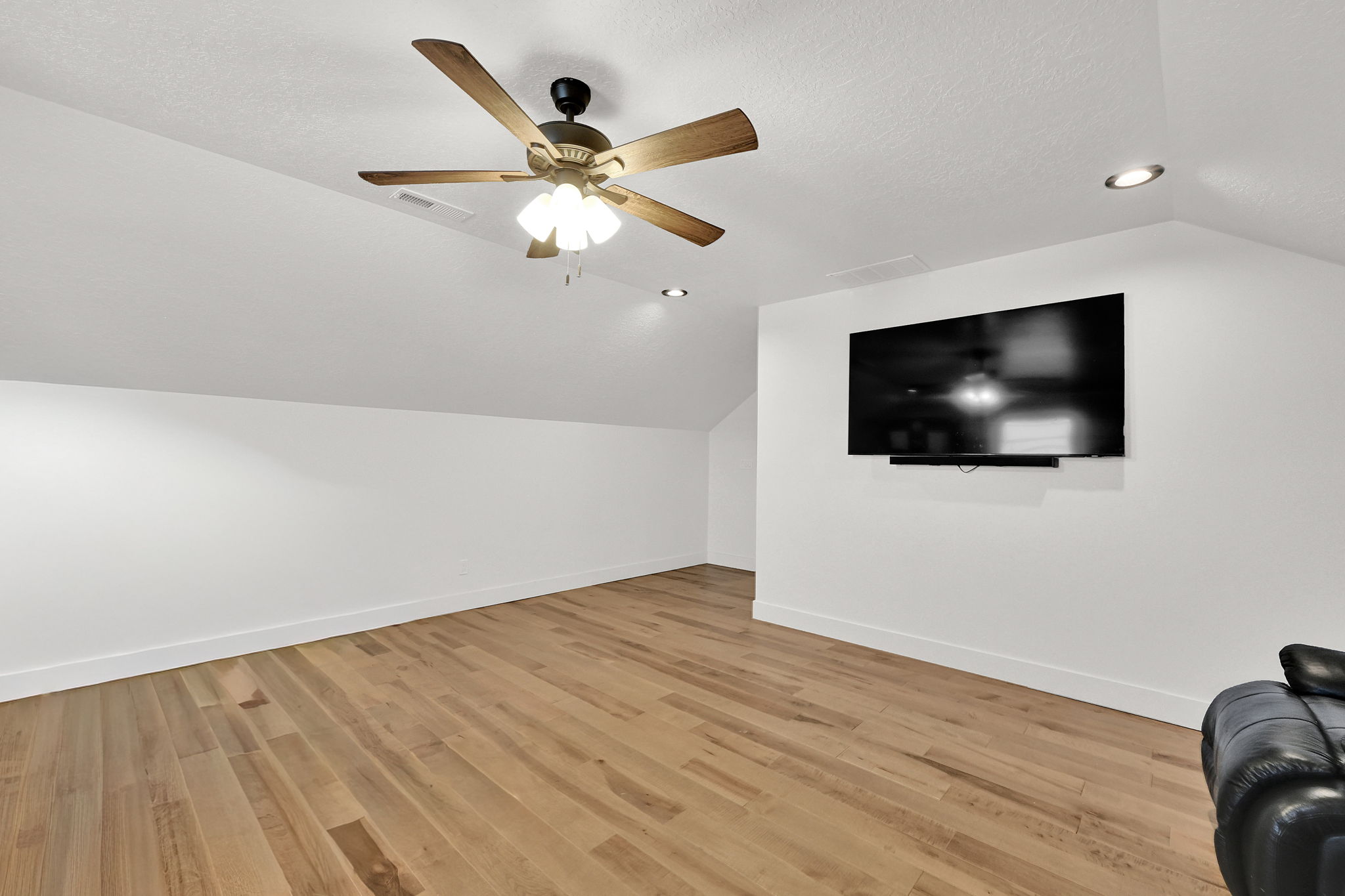 Spacious room featuring wood-finish flooring, white walls, and a sloped ceiling with recessed lighting