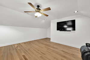 Spacious room featuring wood-finish flooring, white walls, and a sloped ceiling with recessed lighting